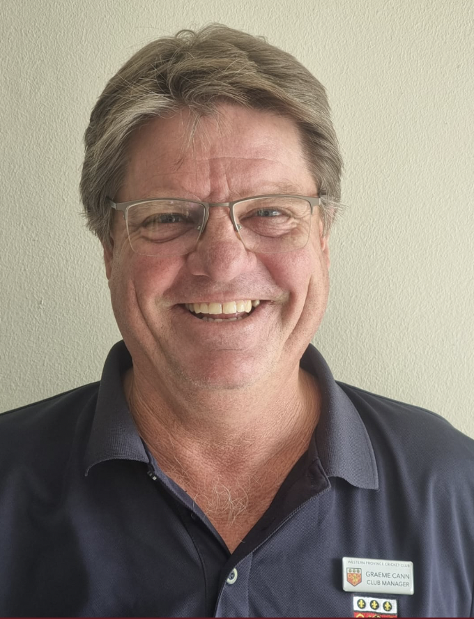 A middle-aged man with glasses and gray hair, smiling and wearing a navy polo shirt with a name tag that reads Graeme Cann, Western Provincial Cricket Club, Club Manager.