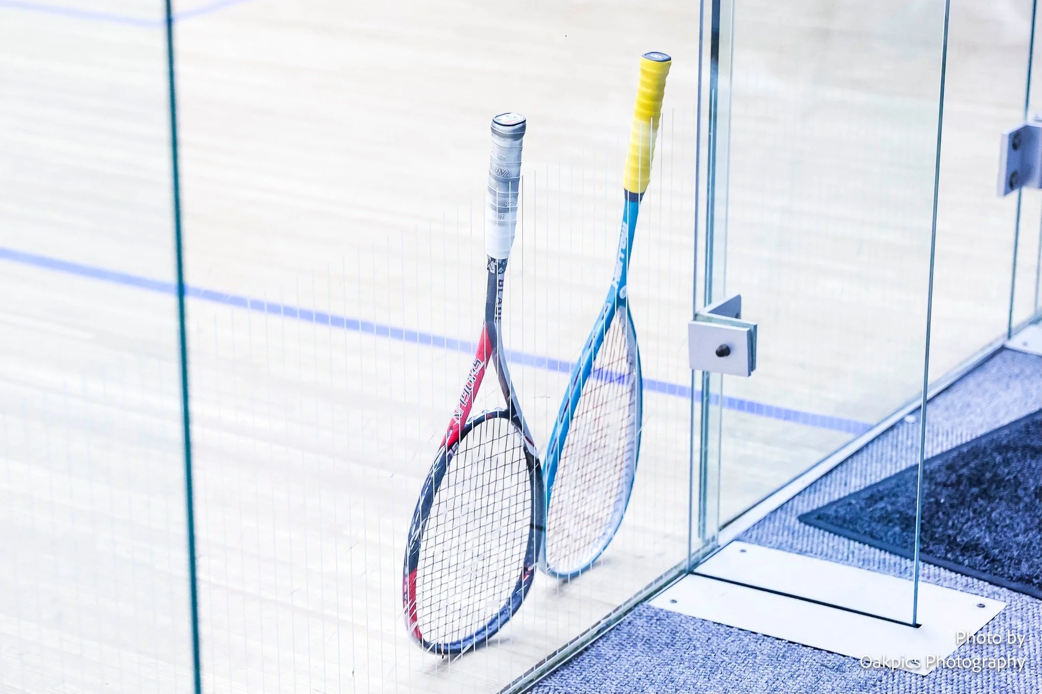 Two tennis rackets leaning against a glass wall on a tennis court.