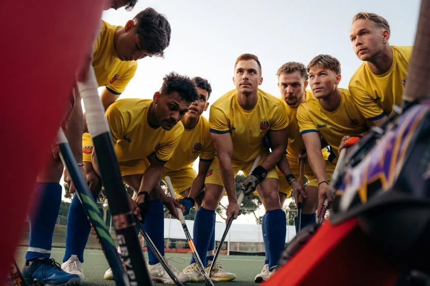 Hockey team in yellow uniforms listening to coach during timeout on field.