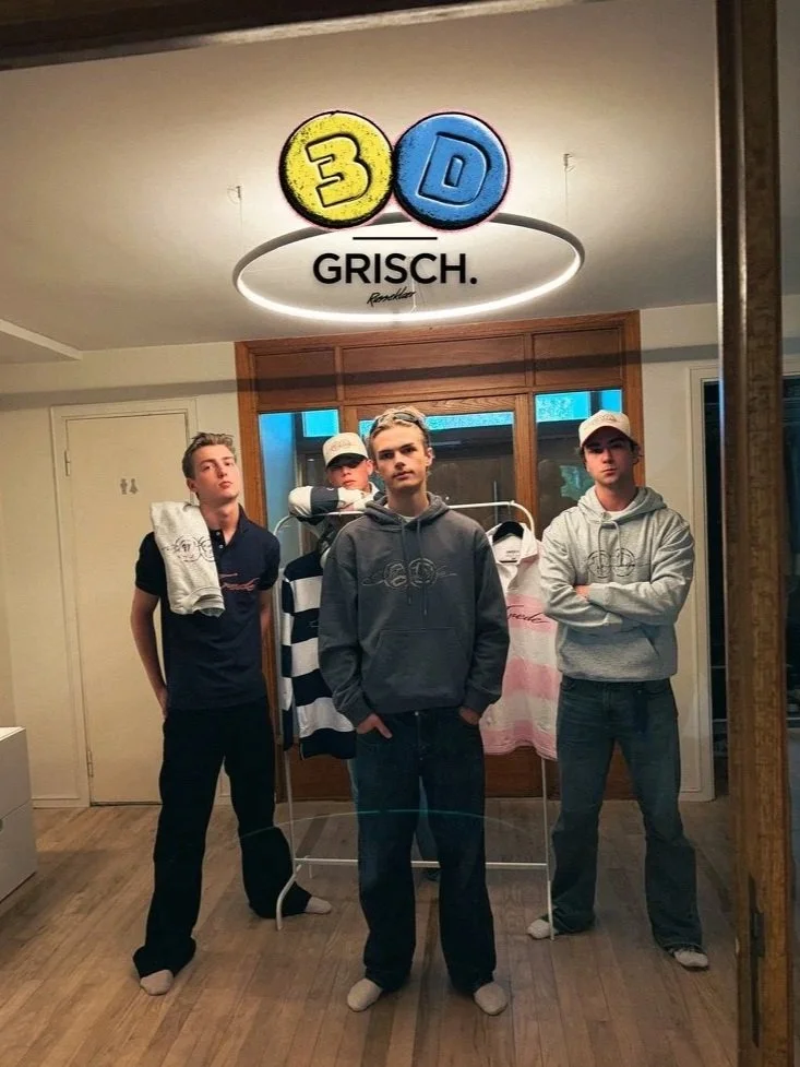 Fire unge menn står foran et klesstativ med klær, i en rom med trevegger og et vindu. Det er en lysekrone med logoen '3D' over dem. Tekst under lysekronen sier 'GRISCH.'