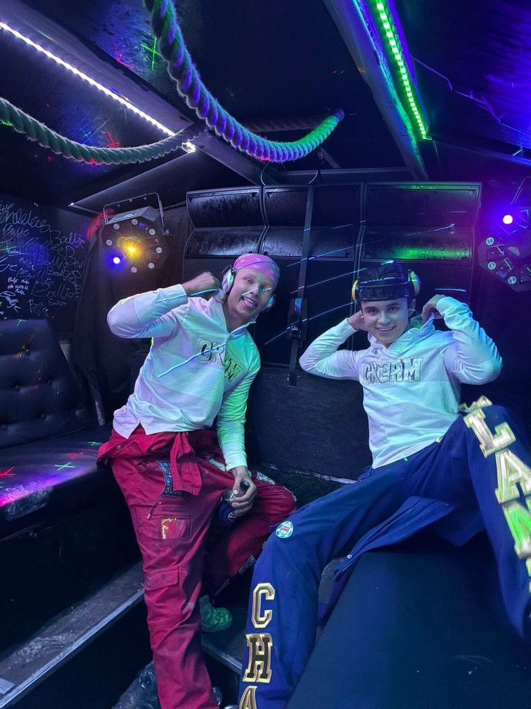To unge mennesker med hodesett i en romhopp-aktivitet med neonlys og fargede lys, smilende og justerende headsetene sine.