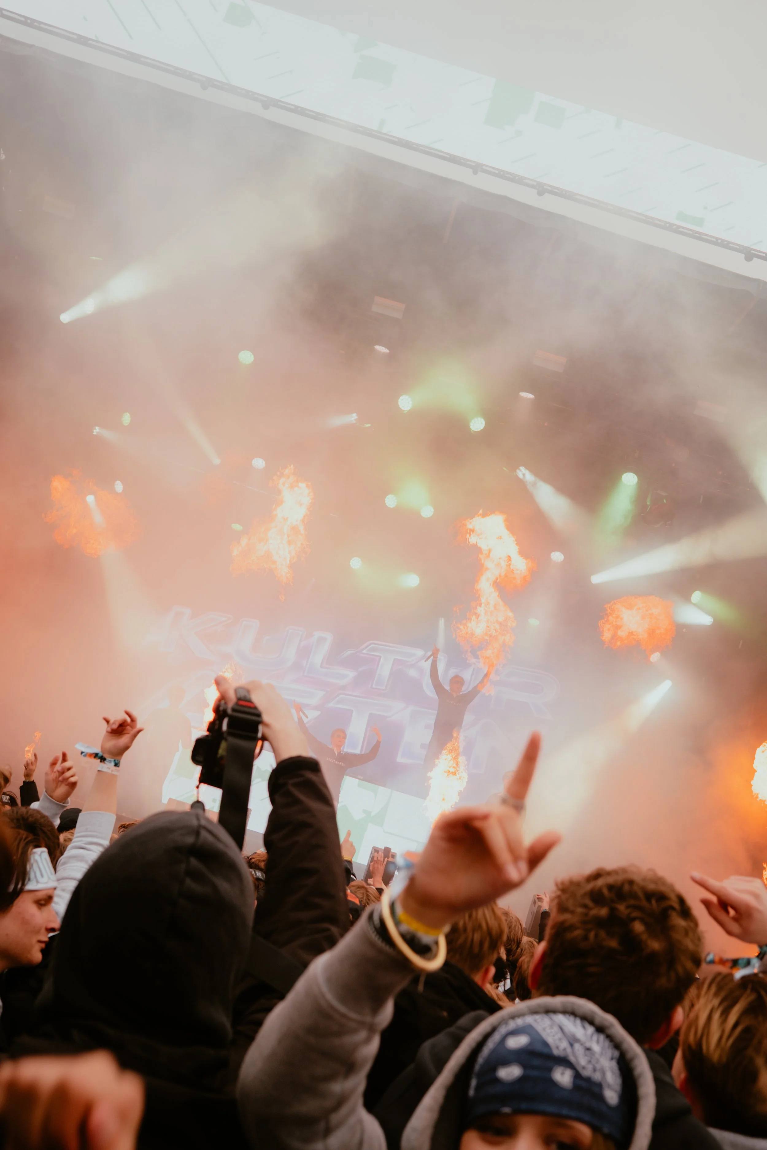 En gruppe mennesker på en konsert med fyrverkeri og lys, der mange har armene i været.