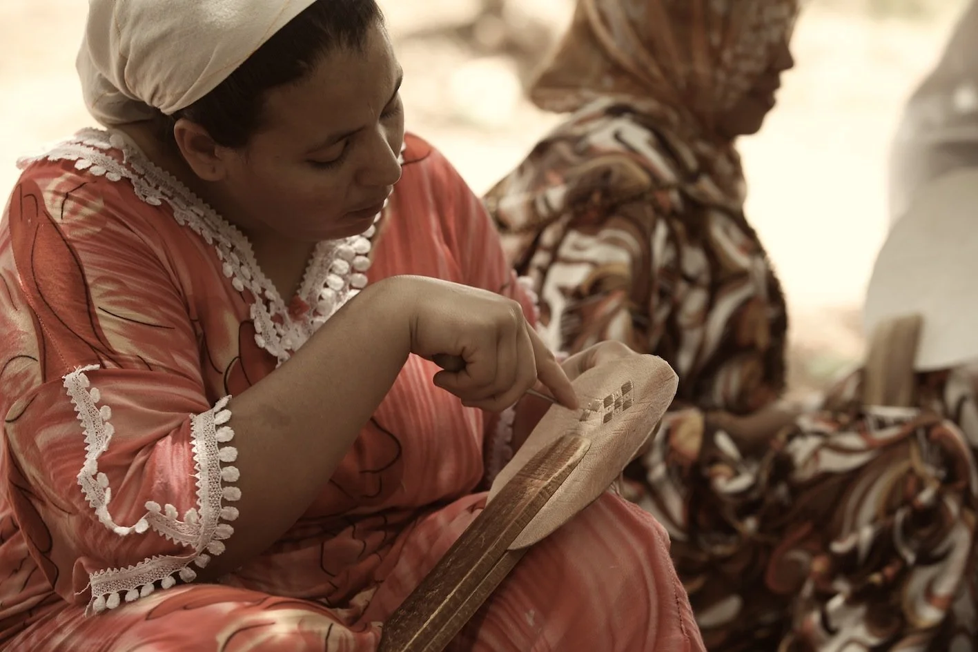 Frauen in traditionellen afrikanischen Kleidern, die auf einer Bank sitzen, eine liest auf einem Holzbrett, während die andere neben ihr sitzt.