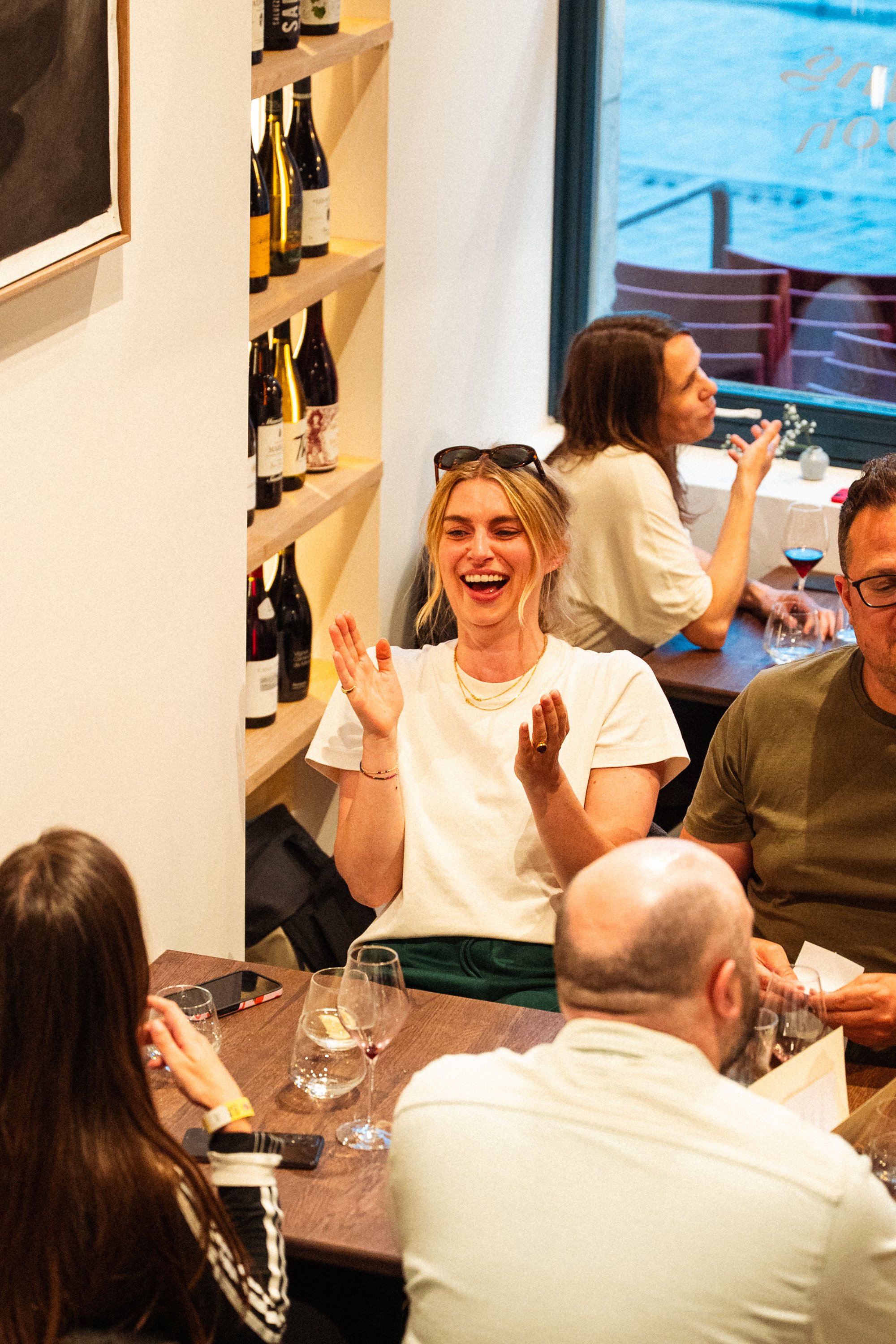 Groep mensen die samen dineert in een restaurant, lachende vrouw in het midden die plezier heeft.