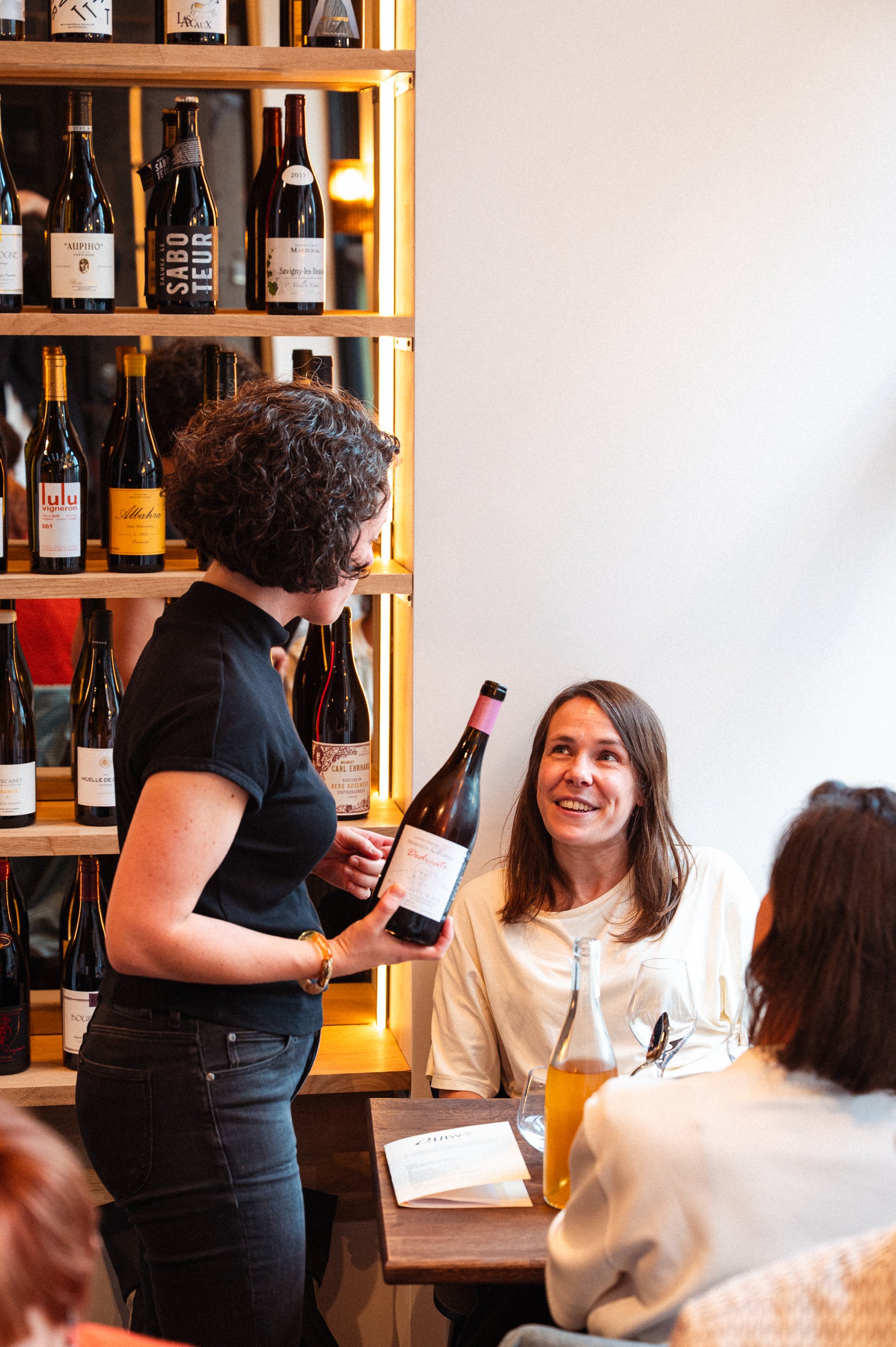 Vrouw die wijn serveert aan een groep mensen in een wijnkroeg of restaurant.