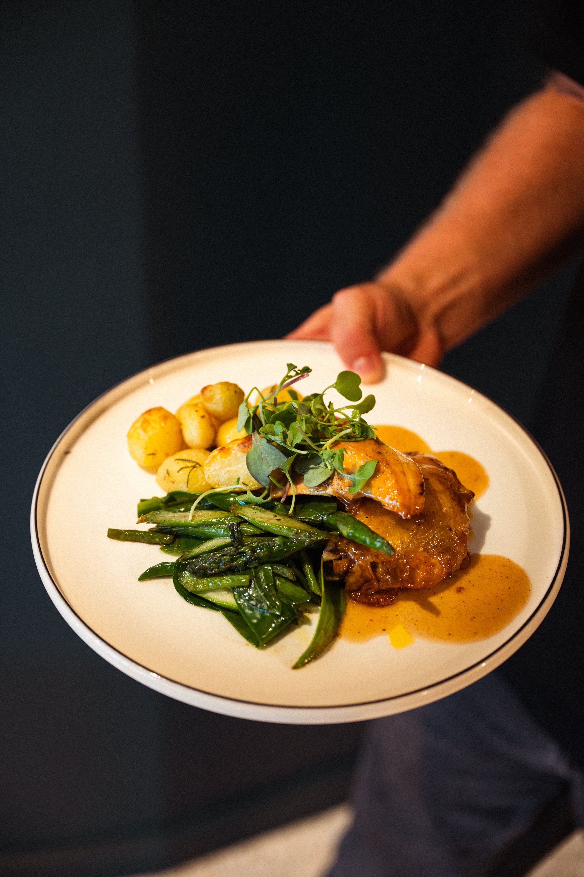 Gevulde groentenschotel met kleine aardappeltjes, groene asperges, en microgroenten op een wit bord, met een saus ernaast.