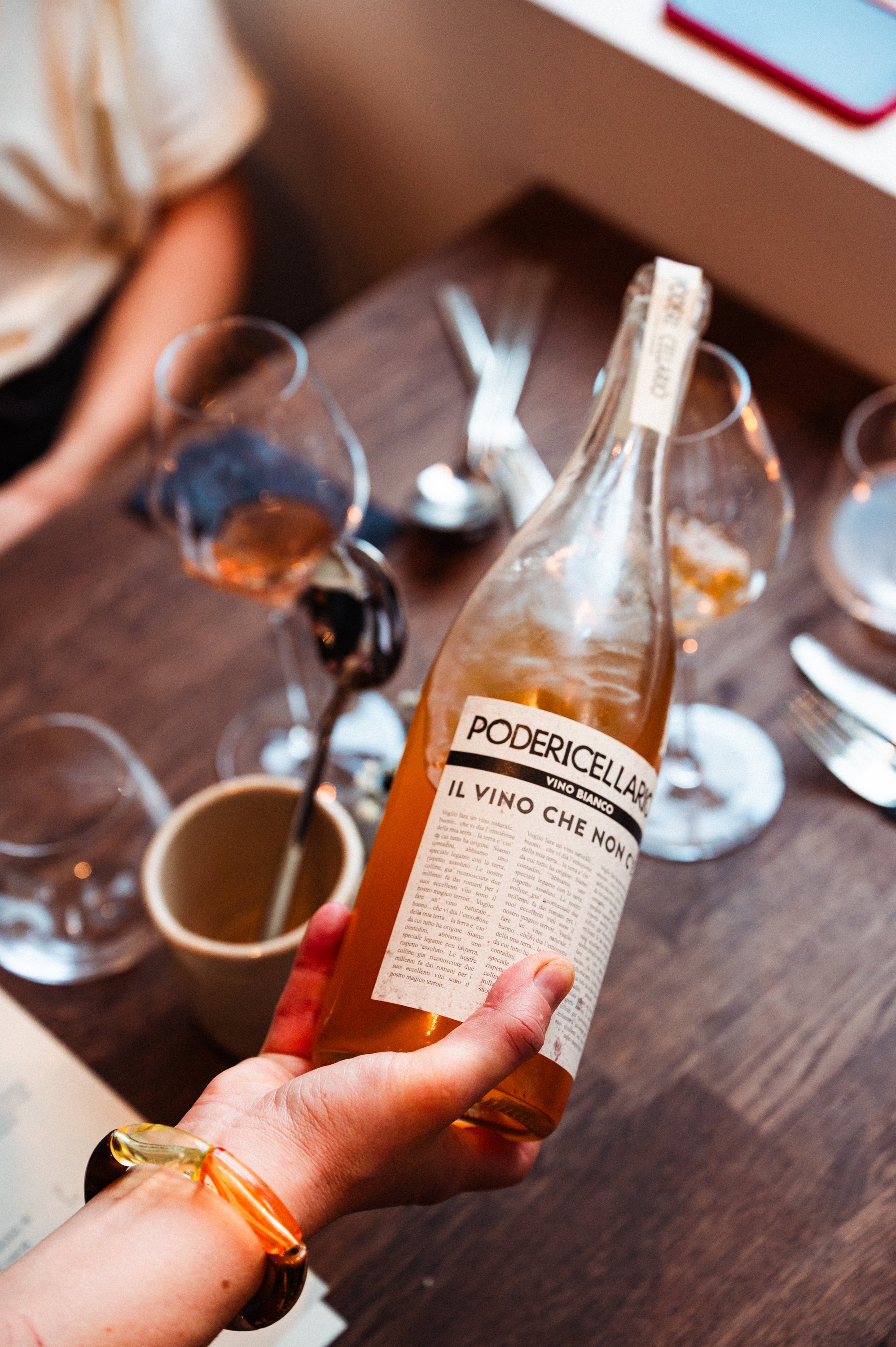 Hand die een fles witte wijn vasthoudt boven een tafel met wijnglazen en bestek.