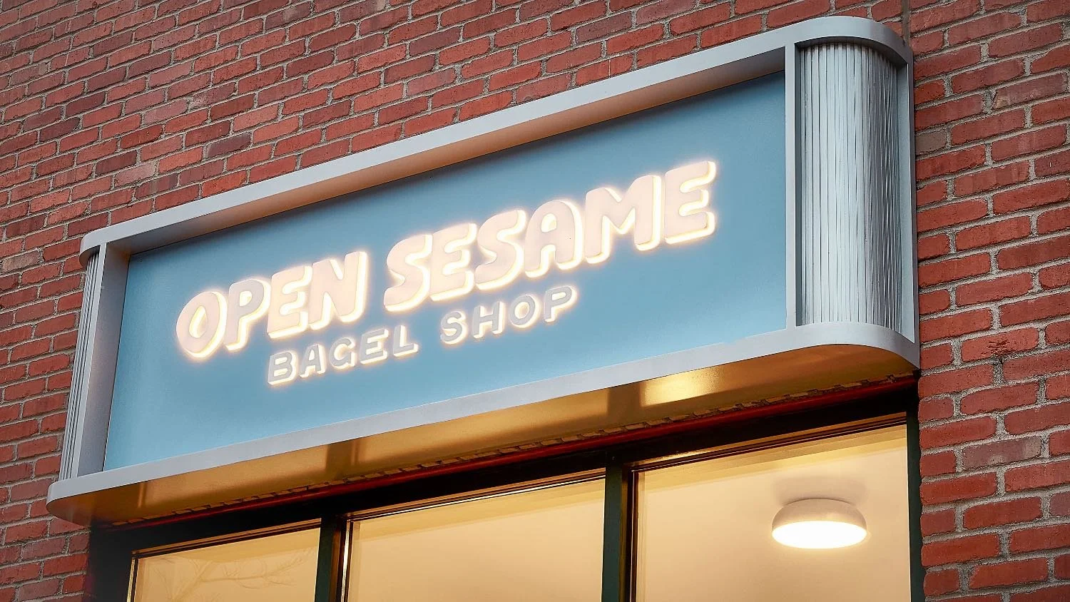 Neon sign for Open Sesame Bagel Shop mounted on a brick building facade.