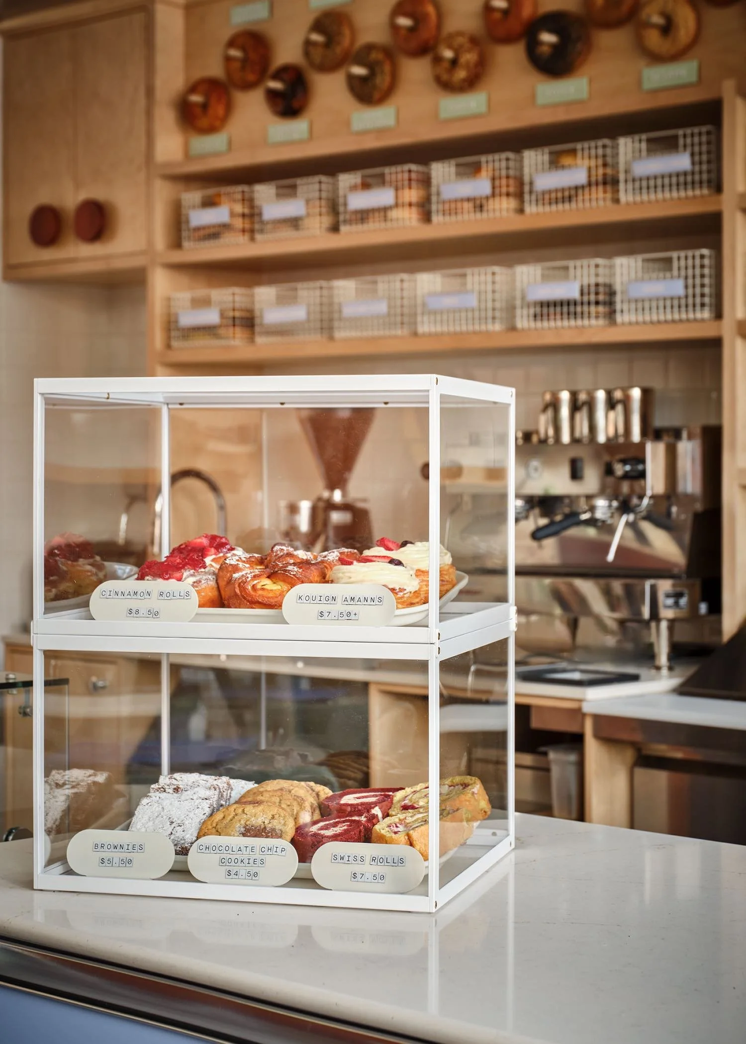 Display case with assorted pastries including cinnamon rolls, kouign amanns, brownies, chocolate chip cookies, and Swiss rolls on a marble countertop at a bakery.