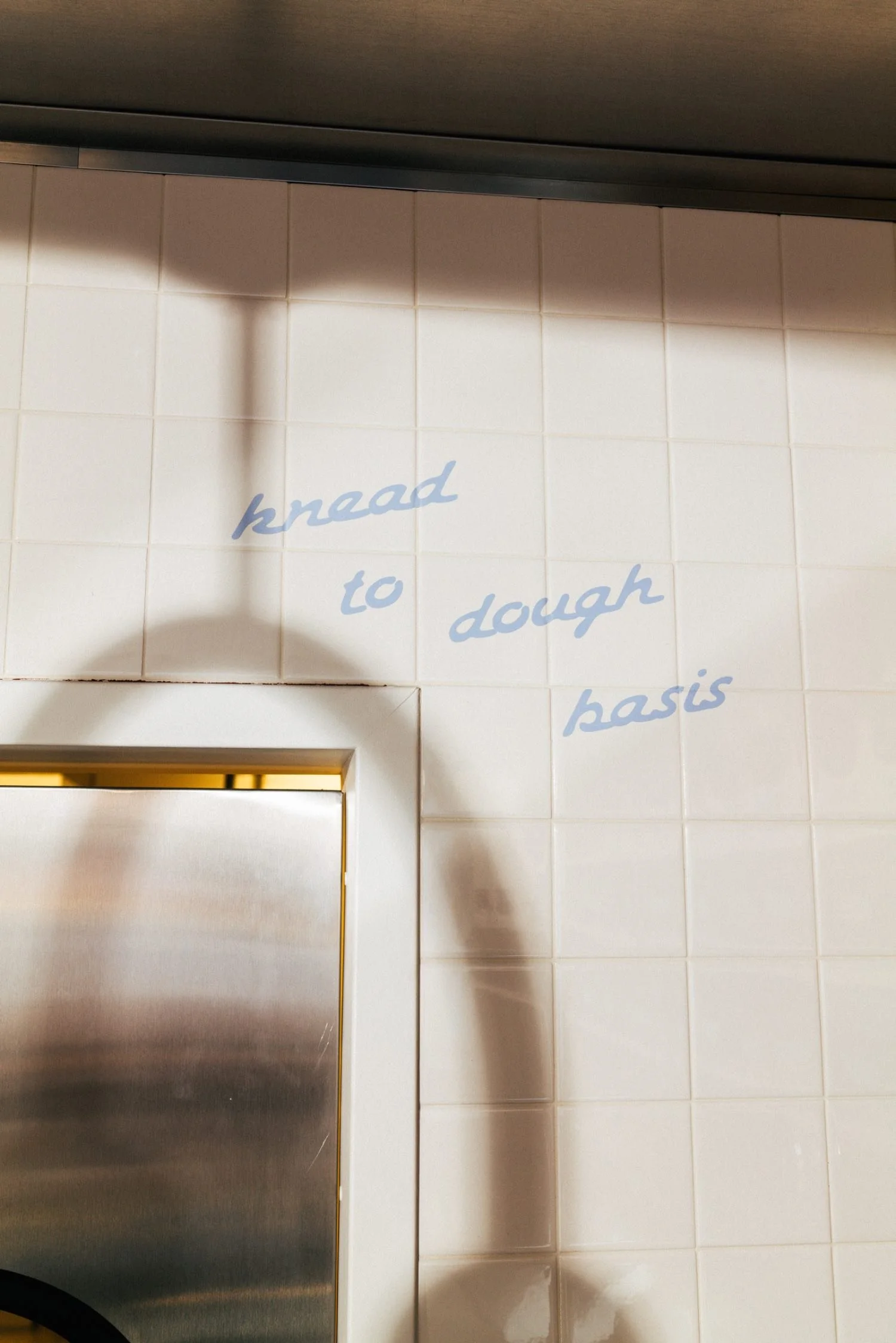 A tiled wall with the phrase 'know to dough basis' written in light blue cursive letters on the tiles.