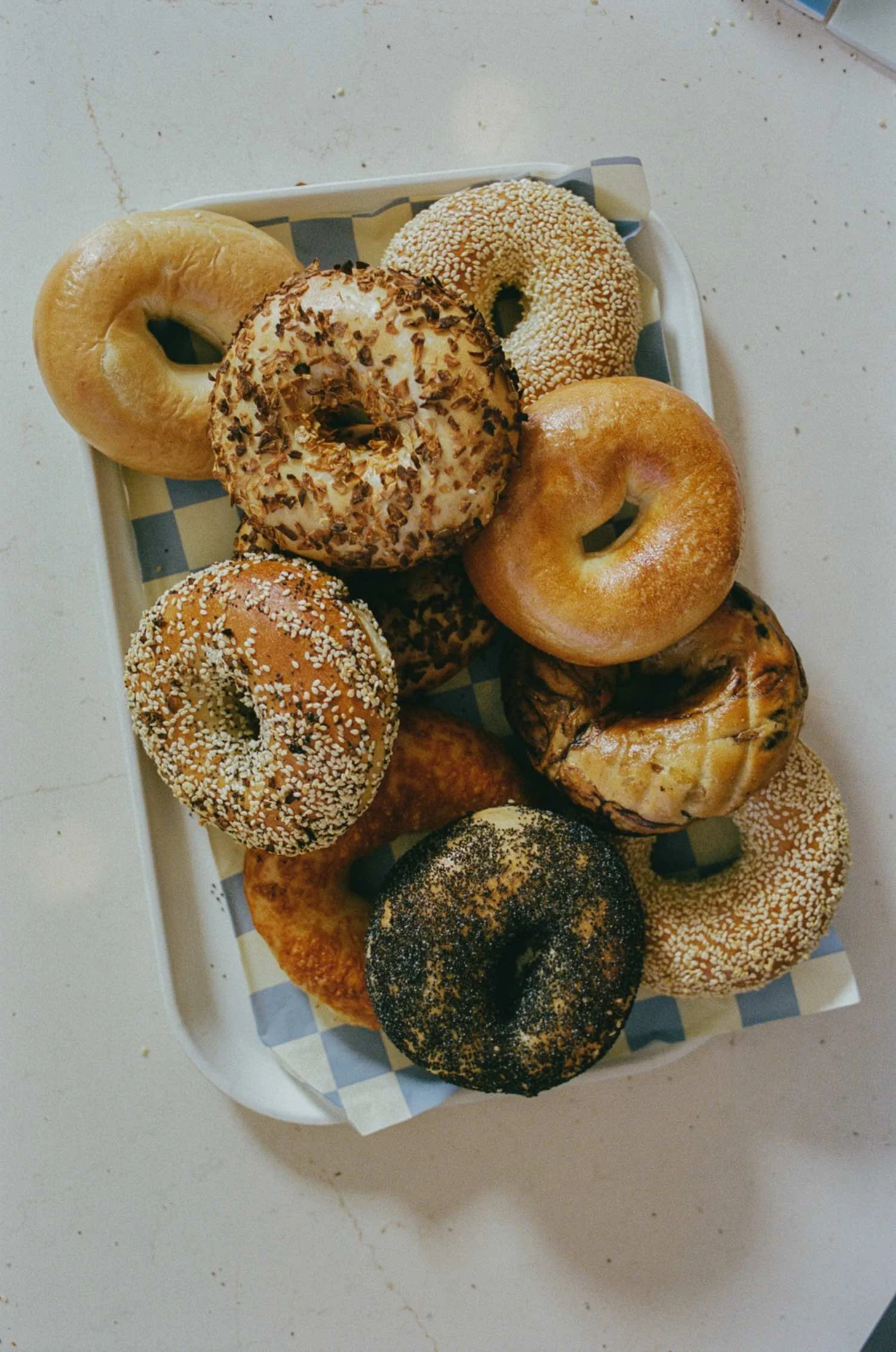 A tray of assorted bagels with various toppings including sesame seeds, poppy seeds, and chopped nuts.