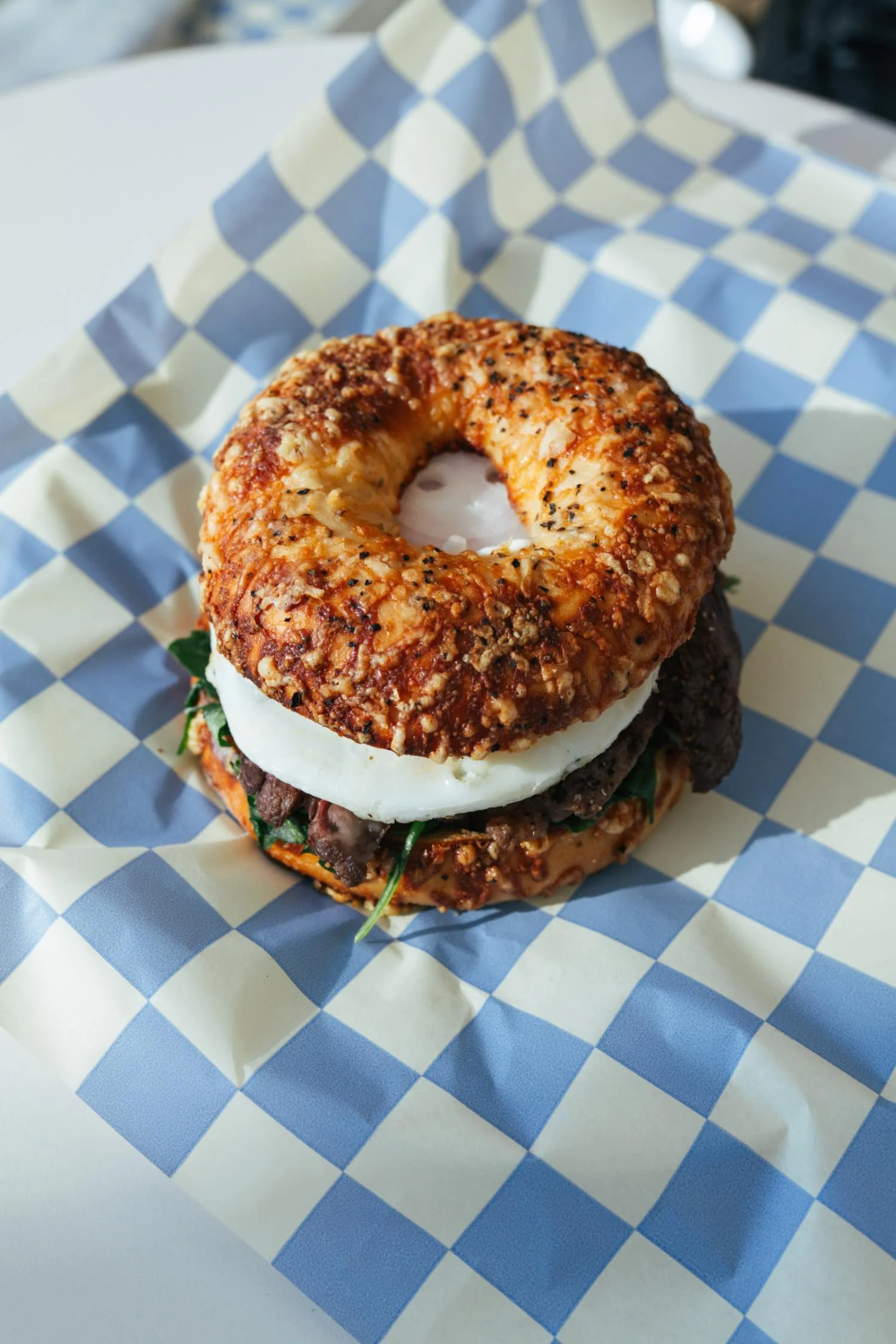 Close-up of a gourmet burger with a toasted bun, cheese, lettuce, and grilled beef patty, served on blue and white checkered paper.