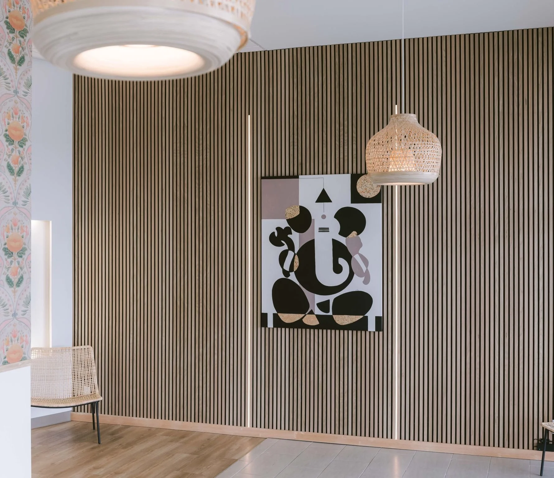 Modern interior created by CM Collaboration construction company; with wood panel wall, abstract black and white artwork, wicker chair, and hanging rattan light fixtures.