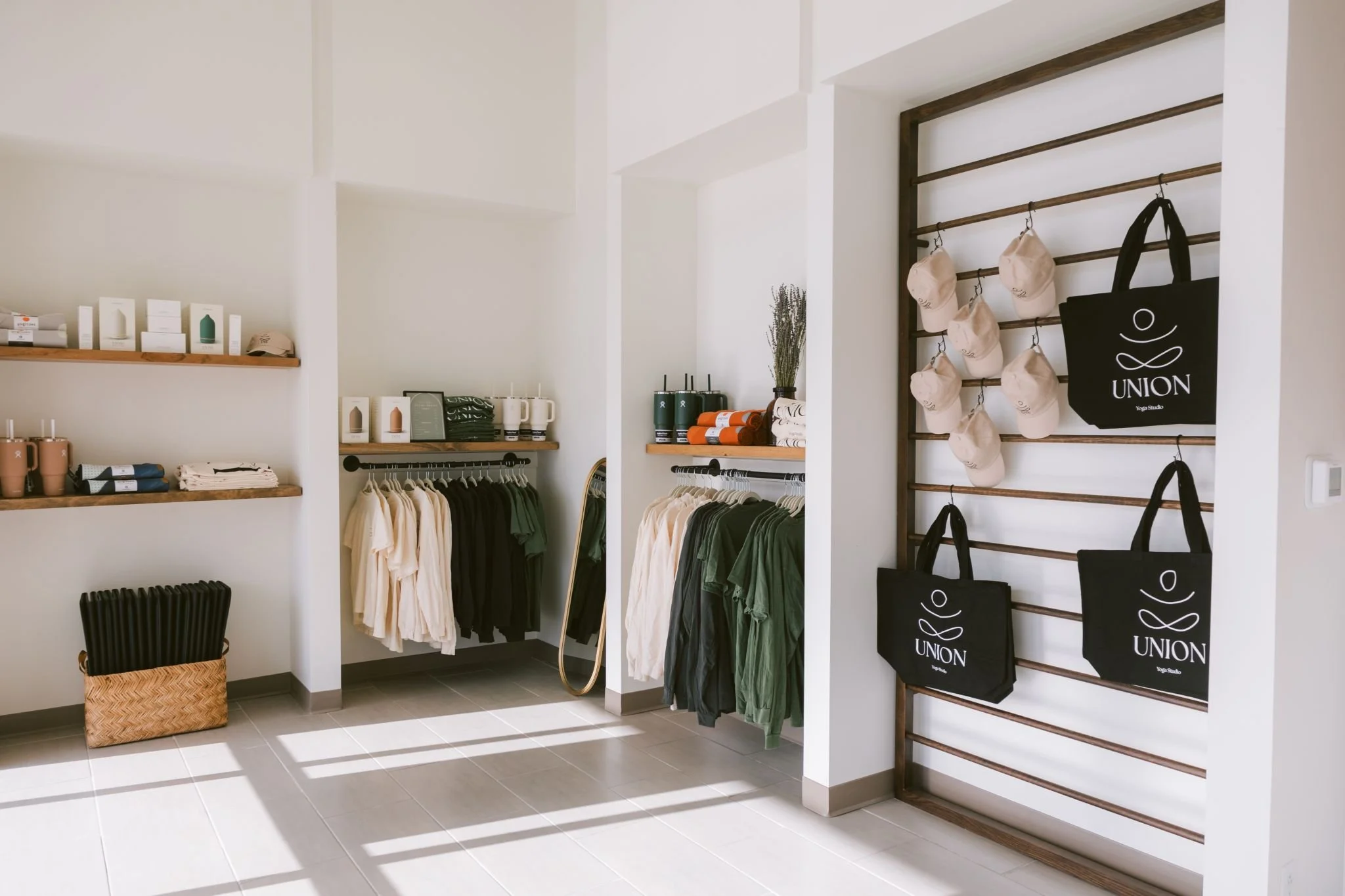 Seamless commercial build-out with no change orders creating a minimalist retail display with clothing on racks, hats, tote bags, and wellness products arranged on shelves in a bright room.