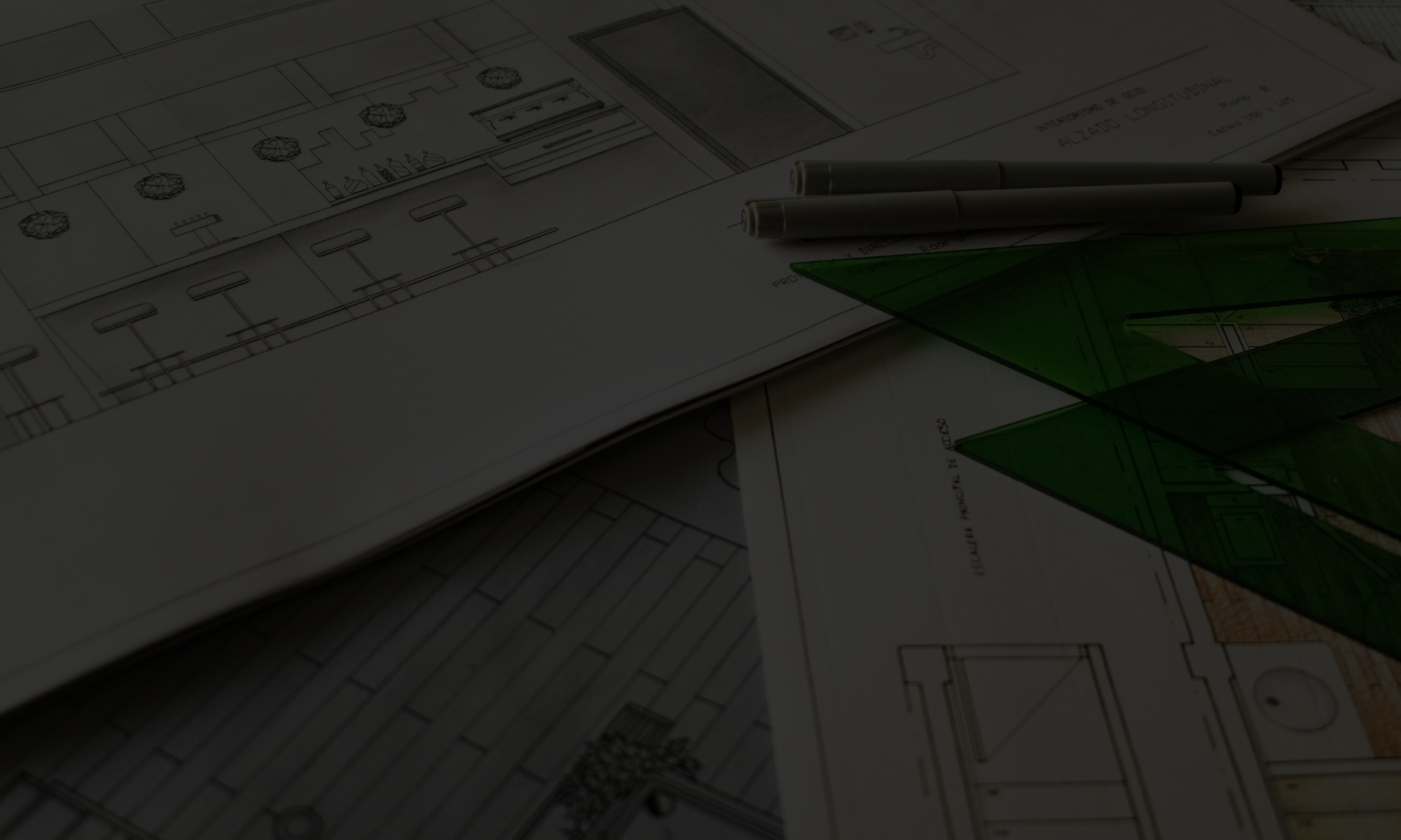 Construction drawings, pens, and a green triangle ruler arranged on a table showing the architectural plans for CM Collaborative.