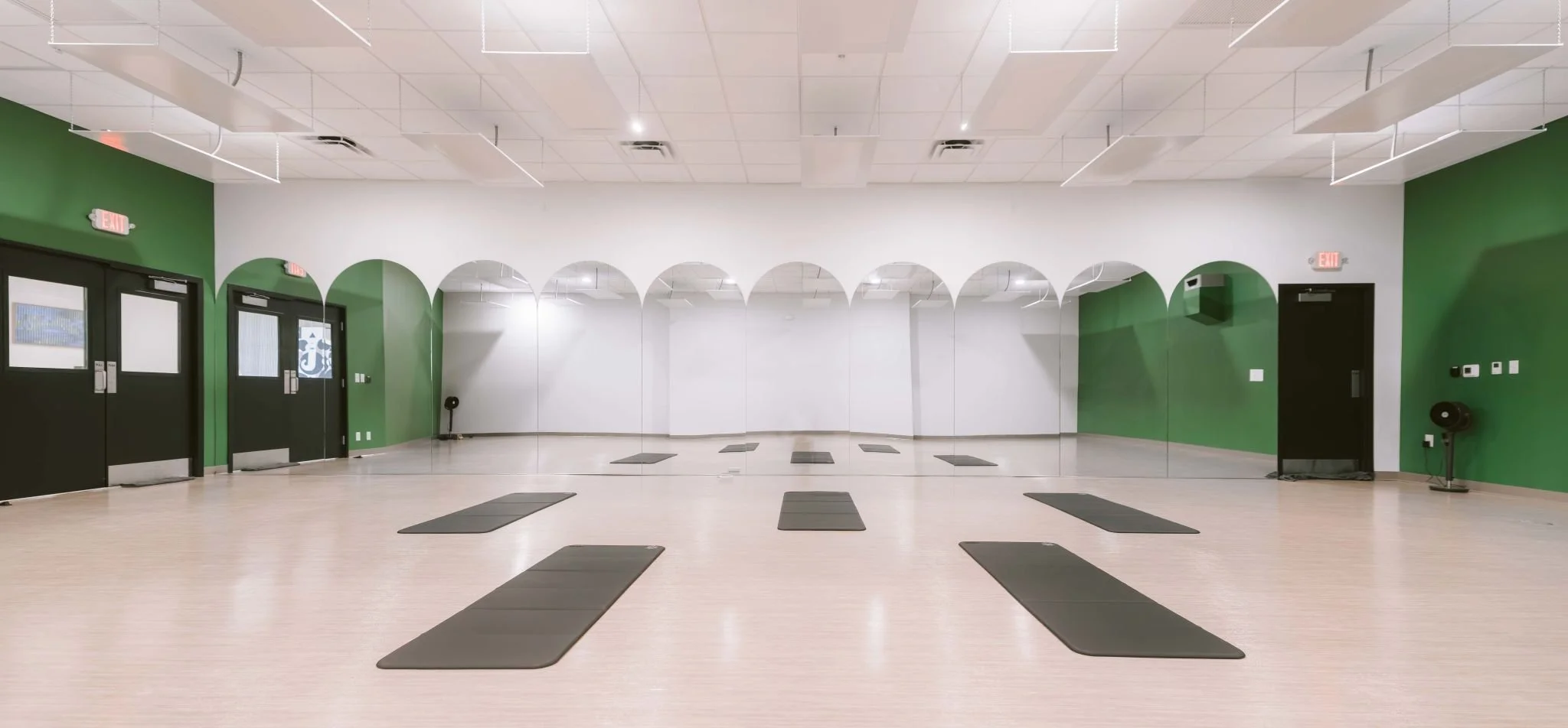 A spacious yoga studio with green walls, mirrors, and black mats arranged on a light wood floor created by a commercial remodel contractor.