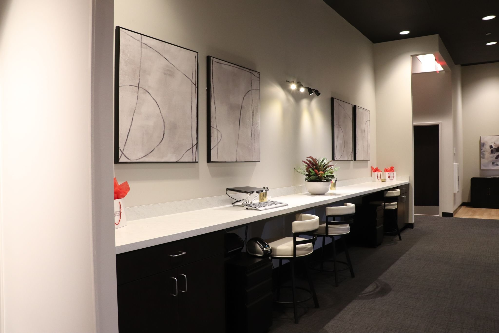 Created by CM Collaboration, a modern office space with a long counter, chairs, abstract art on the wall, and desk accessories.