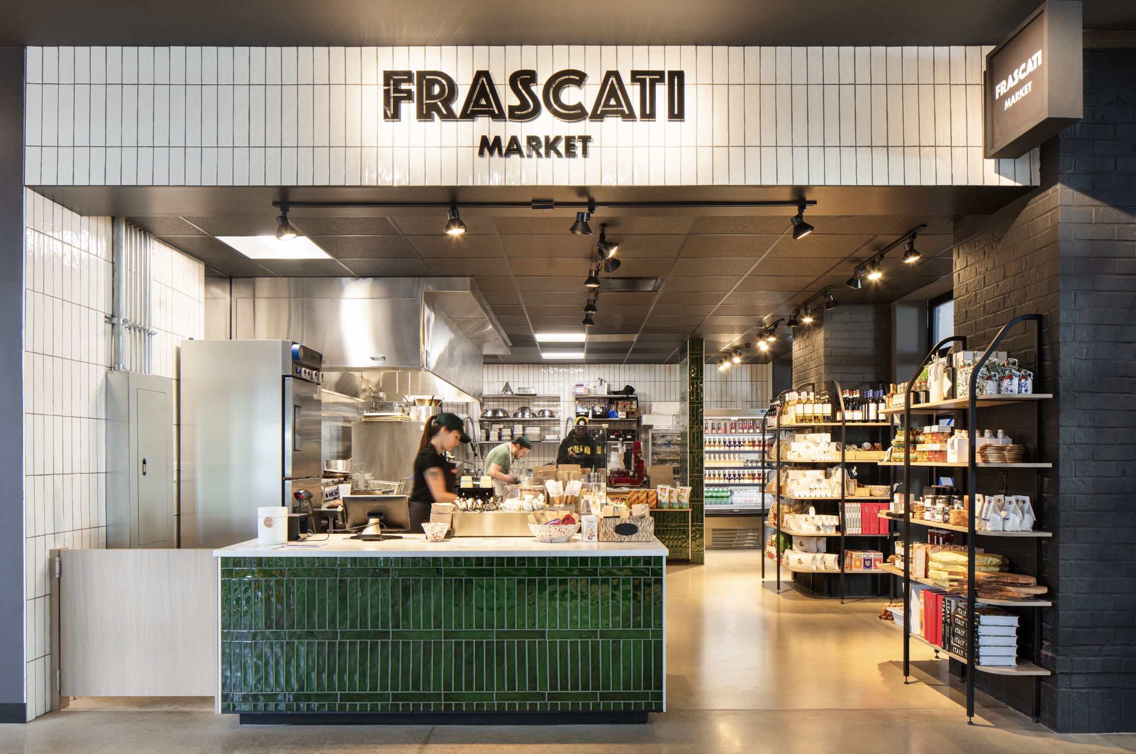 A restaurant construction company showcases a person works behind the counter at Frascati Market, with shelves of products and a kitchen area visible.
