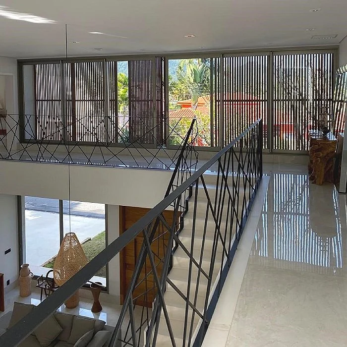 Área de estar moderna com vista para o jardim, vista superior de uma varanda com corrimão preto e uma parede de janelas com persianas de madeira.