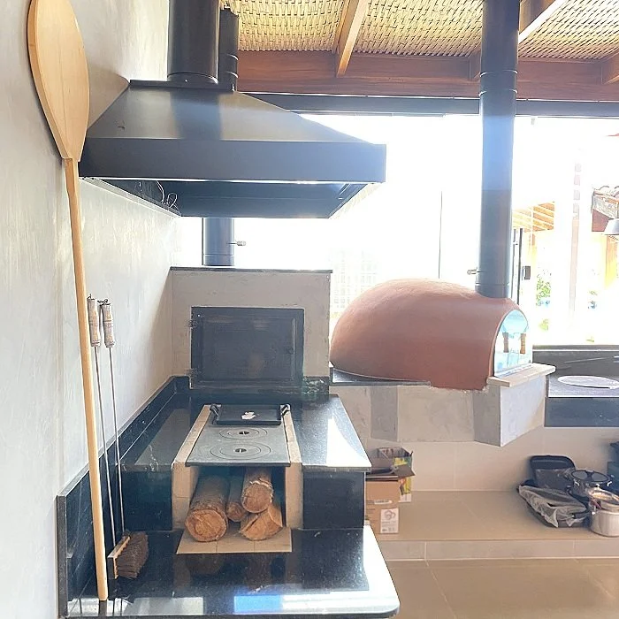 Estufa de uso industrial com forno de pizza de barro ao lado, na cozinha.