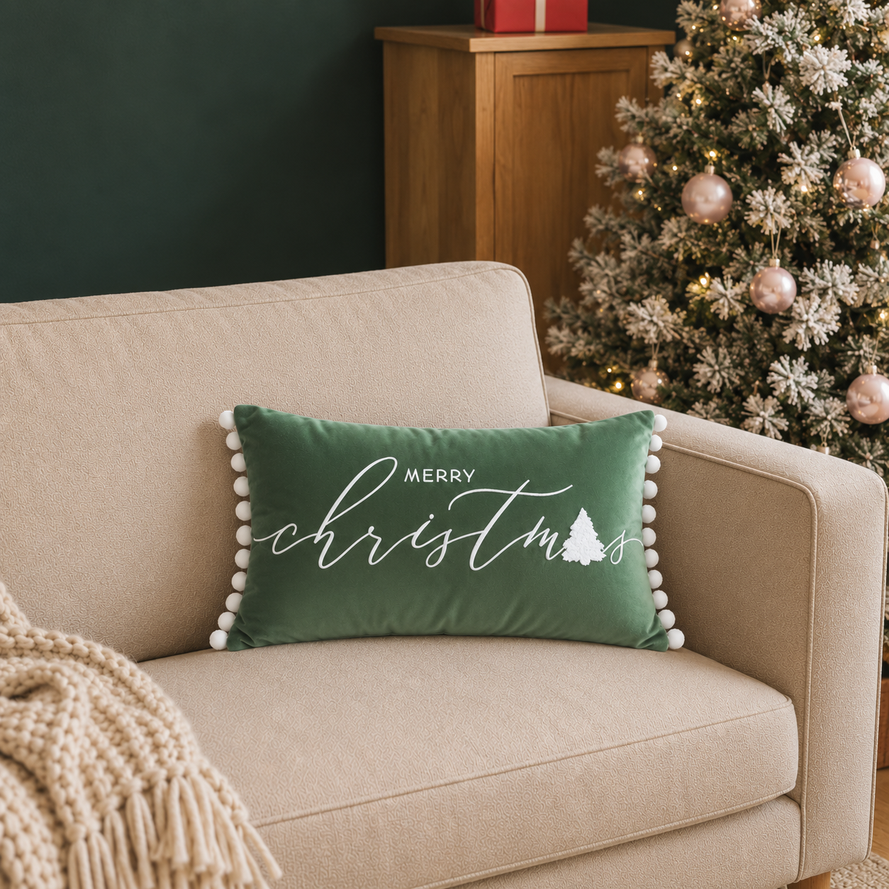 Green Merry Christmas cushion with white lettering and pom pom trim displayed on a sofa