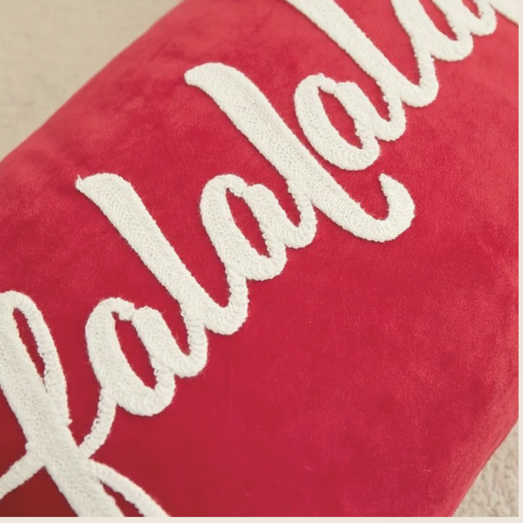 Red Falalalala Christmas cushion with white pom pom trim displayed on a sofa