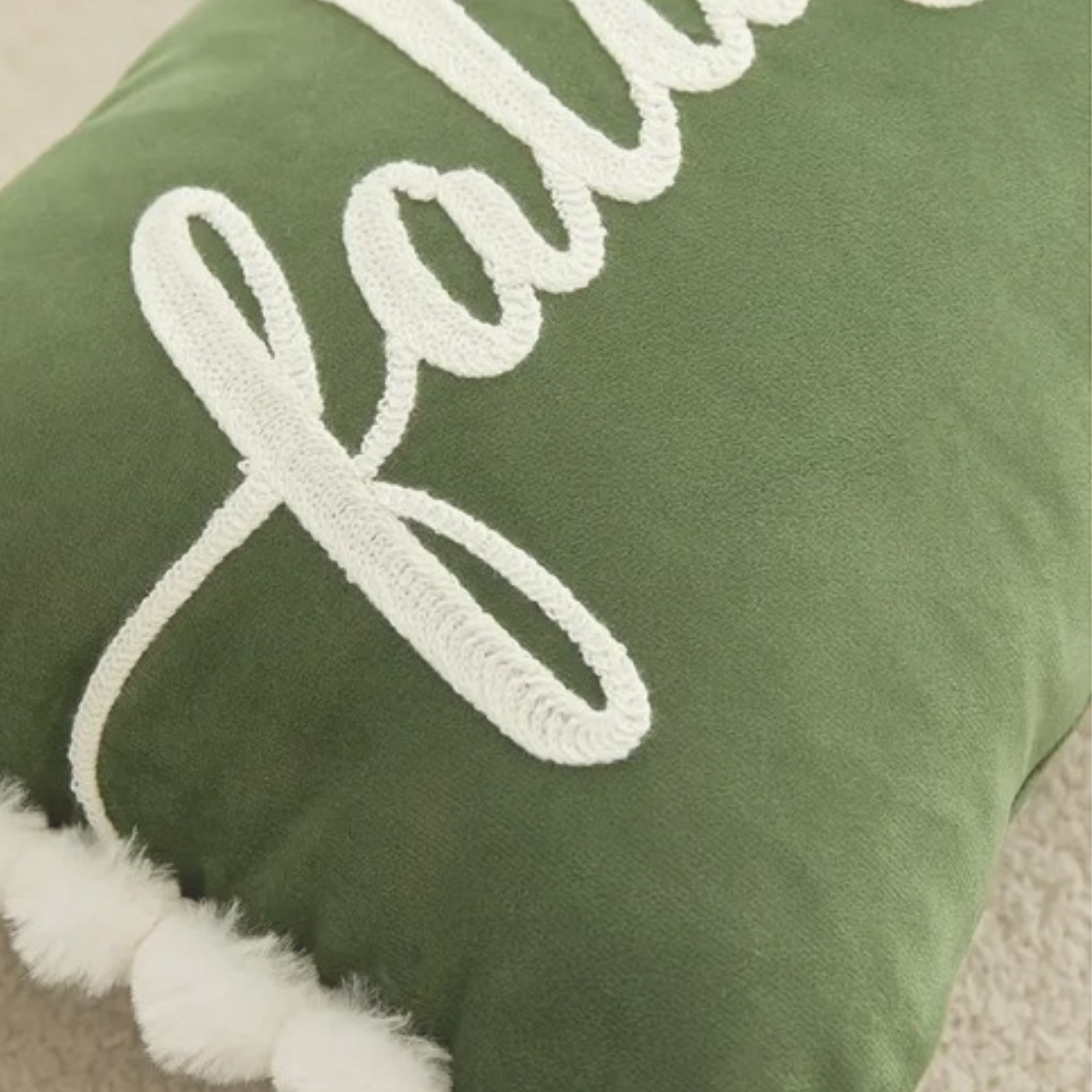 Close-up detail of green Falalalala Christmas cushion with white lettering and pom pom trim