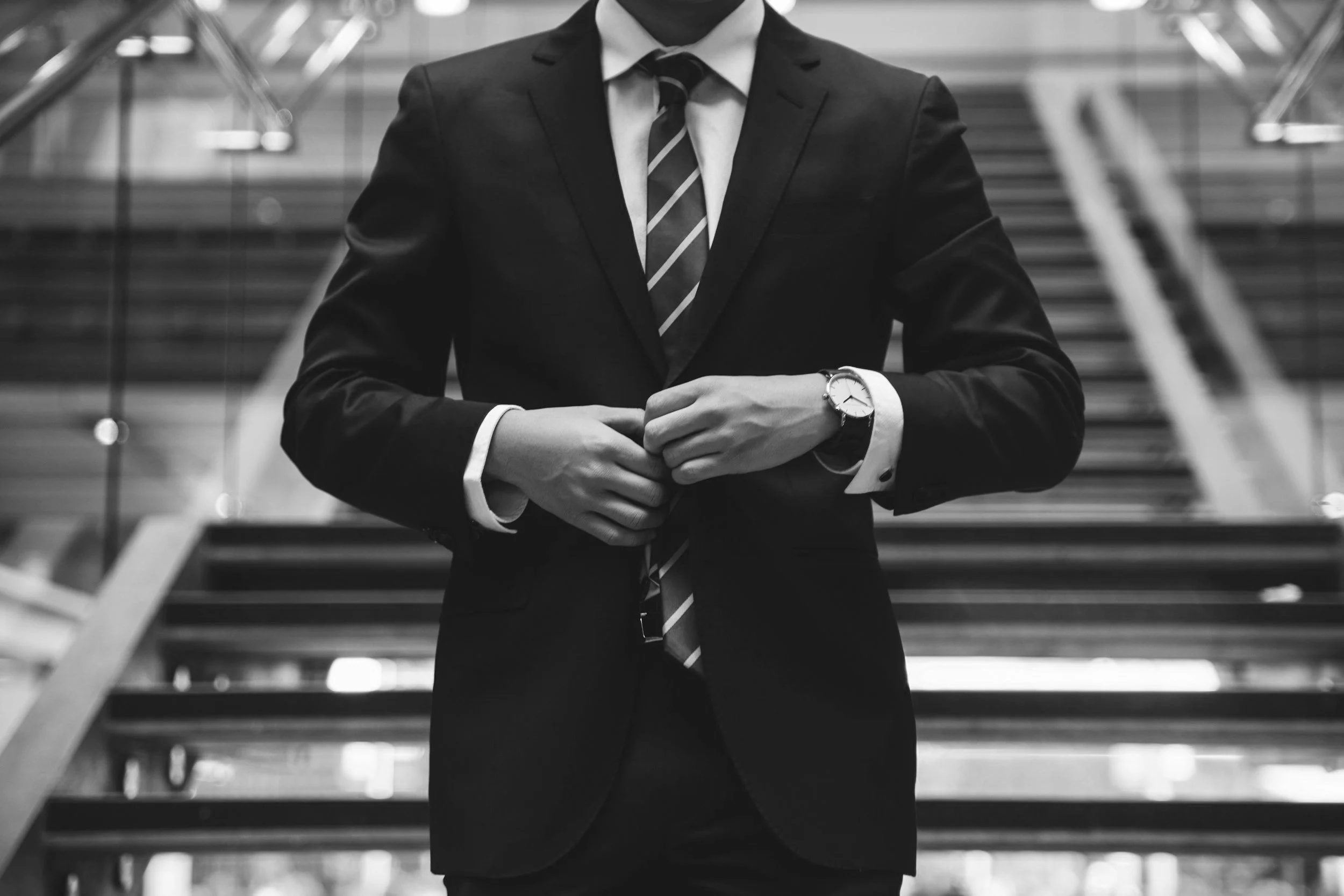 A person in a suit adjusting their jacket, standing on a staircase in an urban environment.