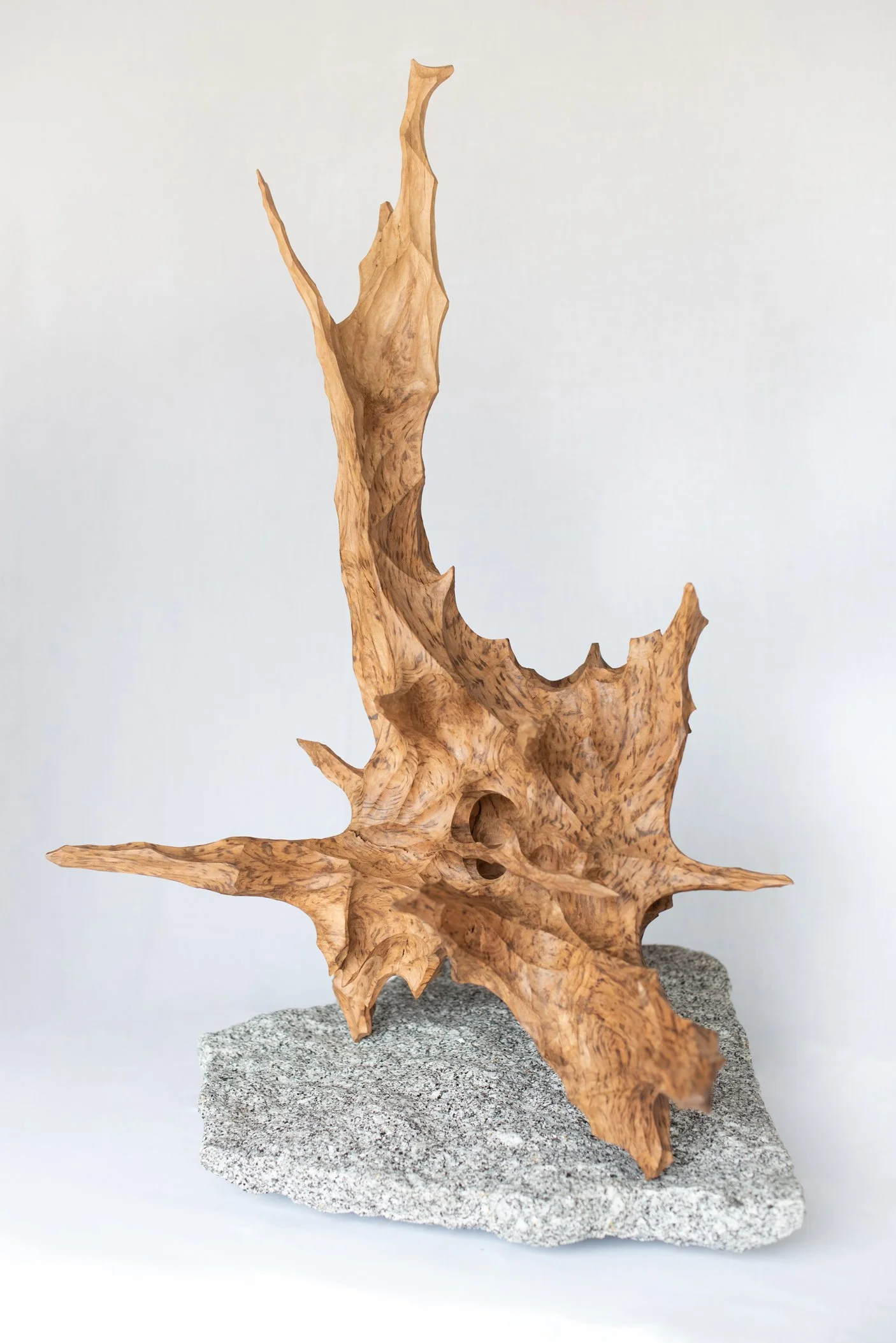 A piece of handcrafted wood sculpture with intricate, natural-looking shapes, mounted on a rough grey stone base.