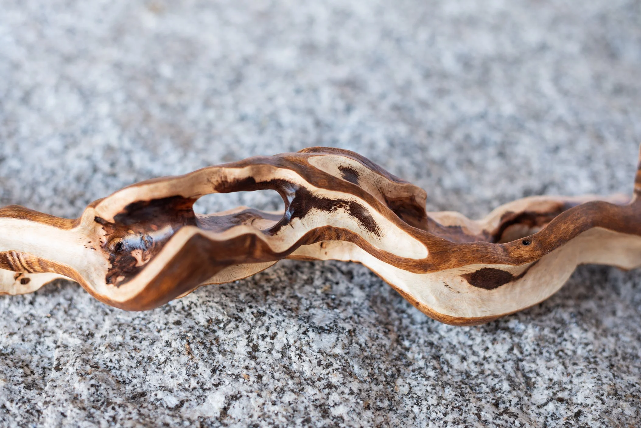 Close-up of a twisted, weathered piece of wood with a natural, irregular shape on a sandy surface.