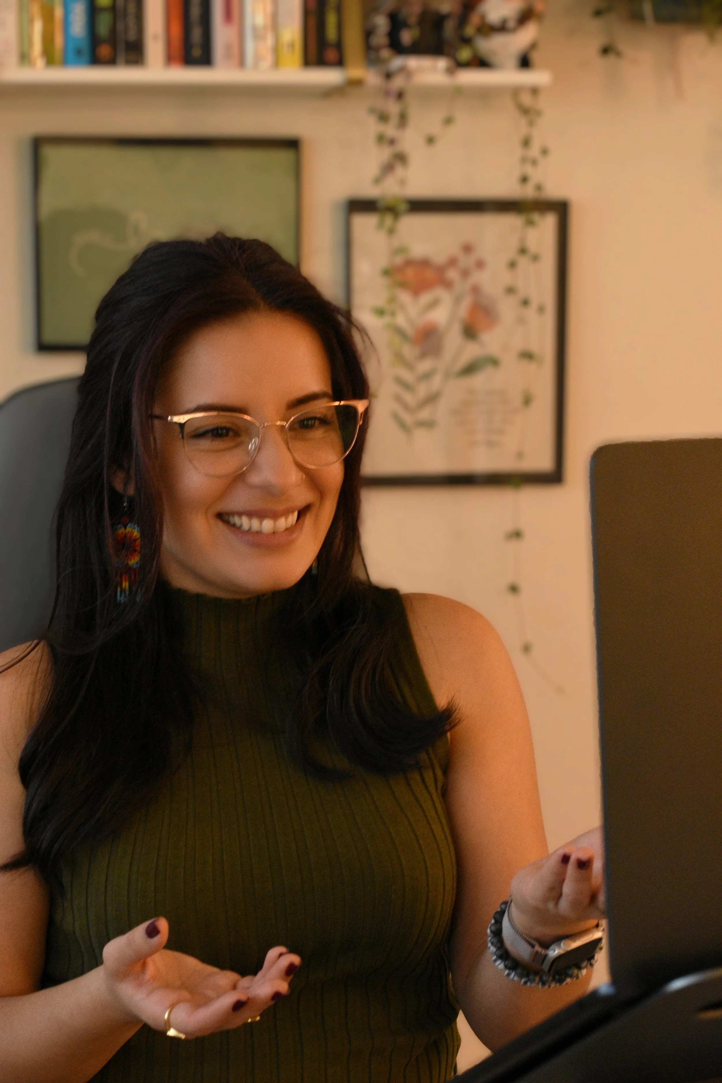 Therapist Lili looking at laptop with a welcoming expression and hand gestures as though in a virtual therapy session