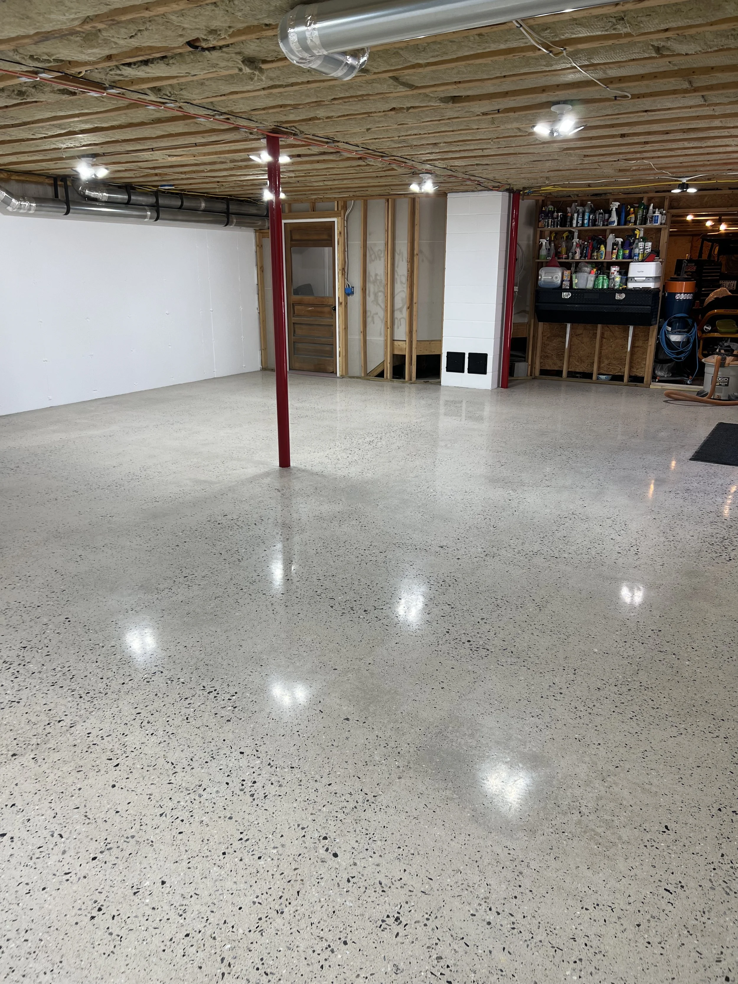 Empty and polished concrete basement floor with exposed ceiling beams and ductwork, wooden walls, and a tool storage area.