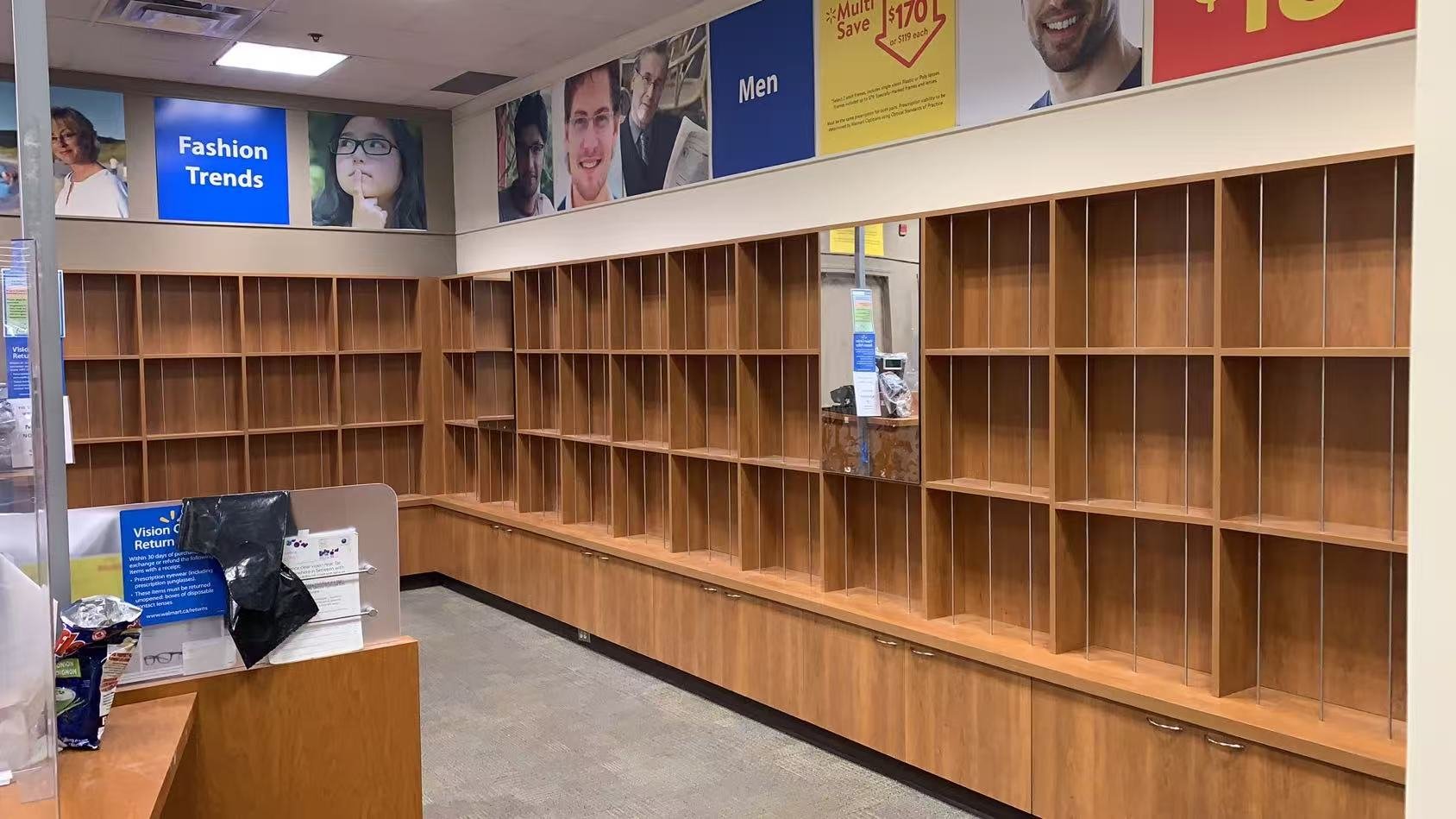 Empty wooden store shelves with small cubbies at a retail store, with some advertisements on the wall above, including signs for fashion trends, men's clothing, and discounts.