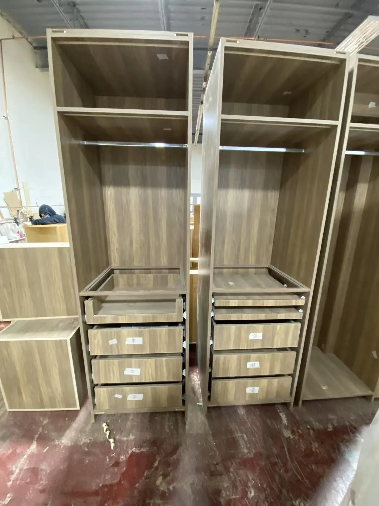 Two large wooden wardrobe units with multiple shelves and drawers, standing upright in a warehouse setting.