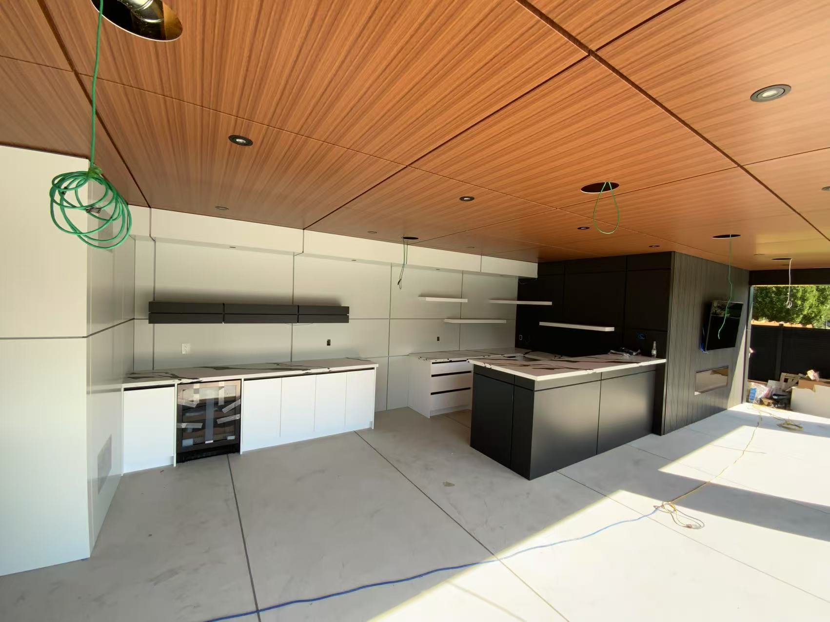 Kitchen under construction with white and black cabinetry, open shelving, and a wood-paneled ceiling.