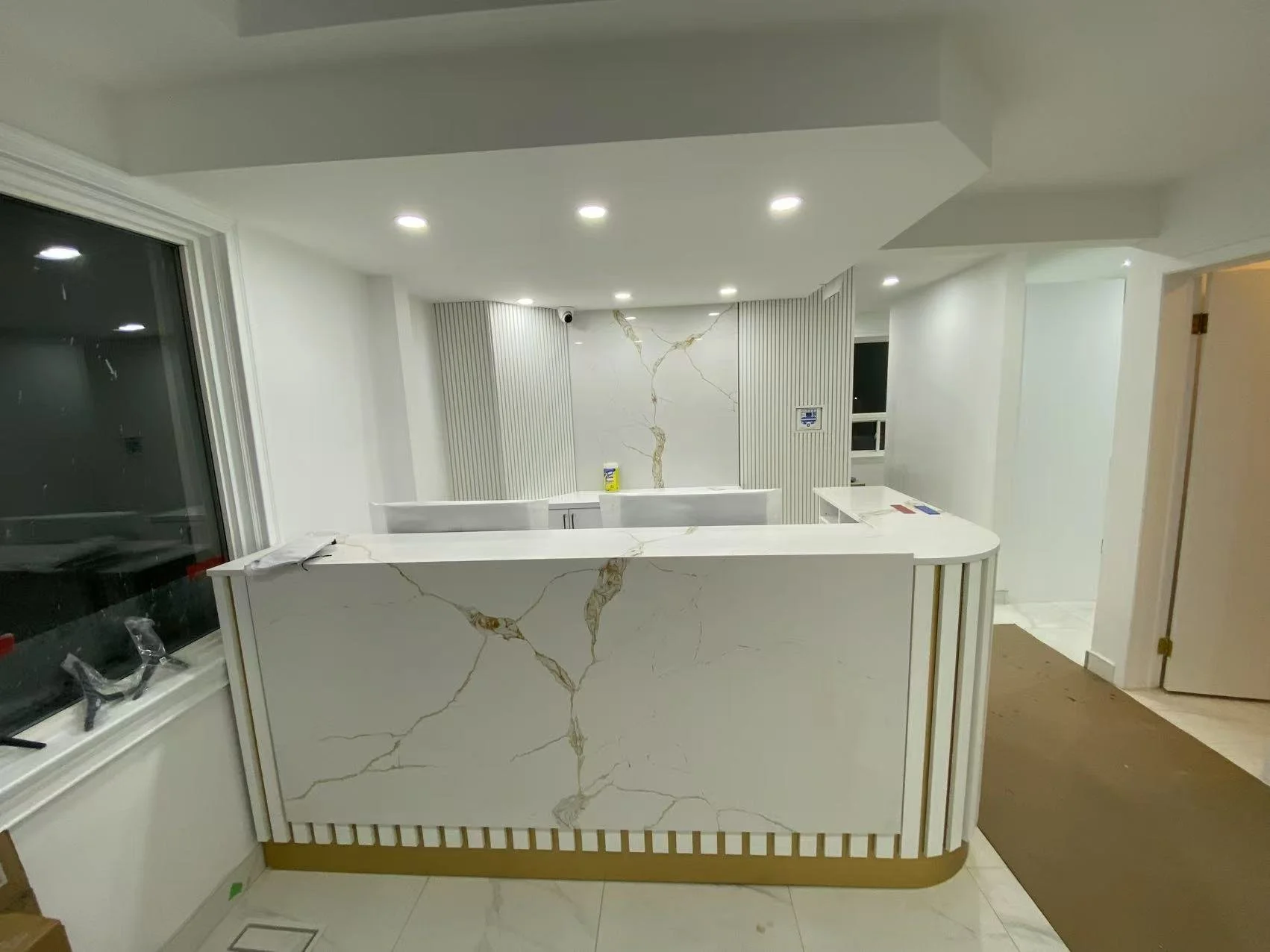 Modern reception or front desk area with white marble design, gold accents, and recessed lighting in a contemporary interior space.