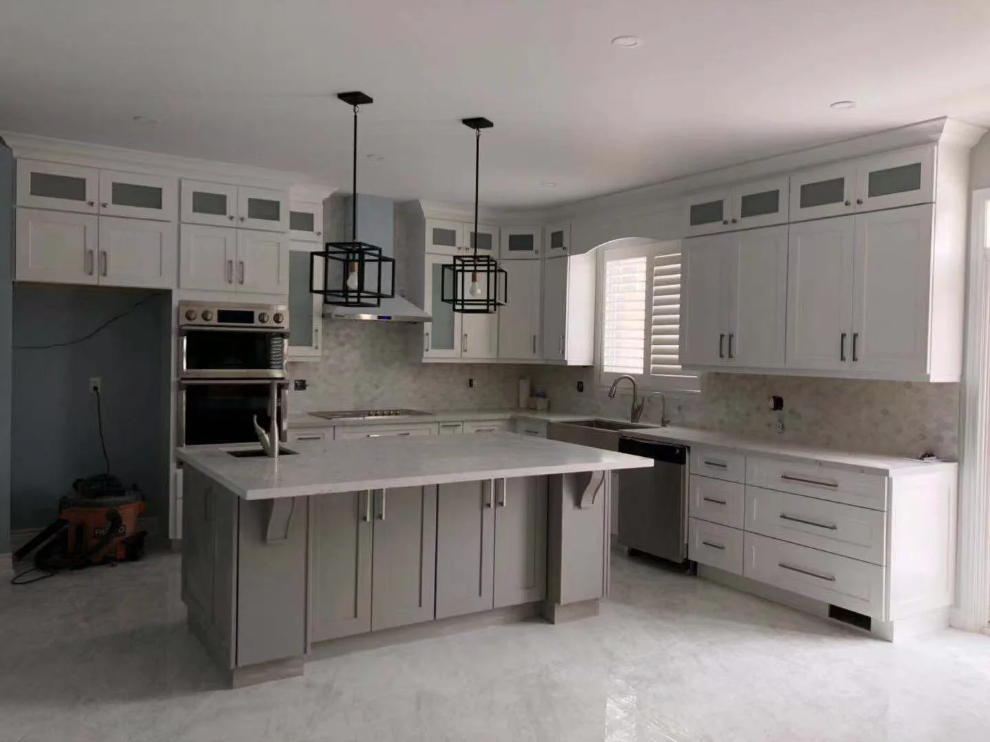 Modern kitchen with white cabinets, marble countertops, a central island, and pendant lighting fixtures.