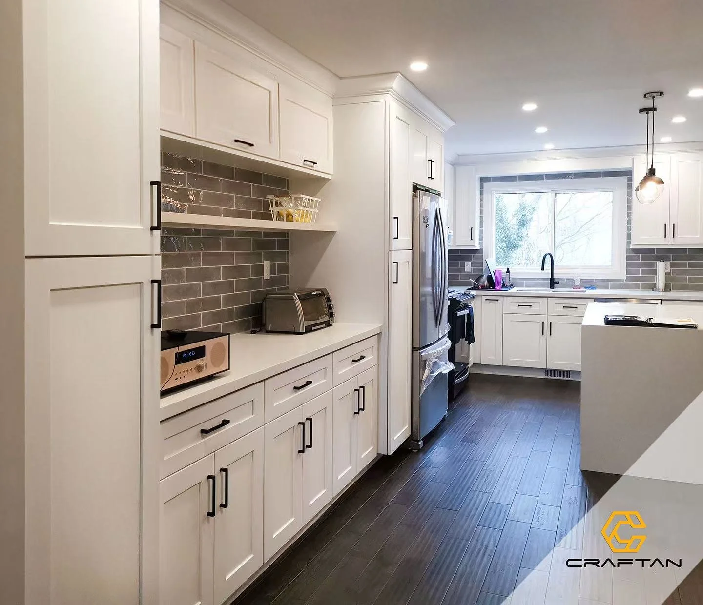 Modern kitchen with white cabinets, dark wood flooring, stainless steel appliances, gray tiled backsplash, and a large window above the sink.