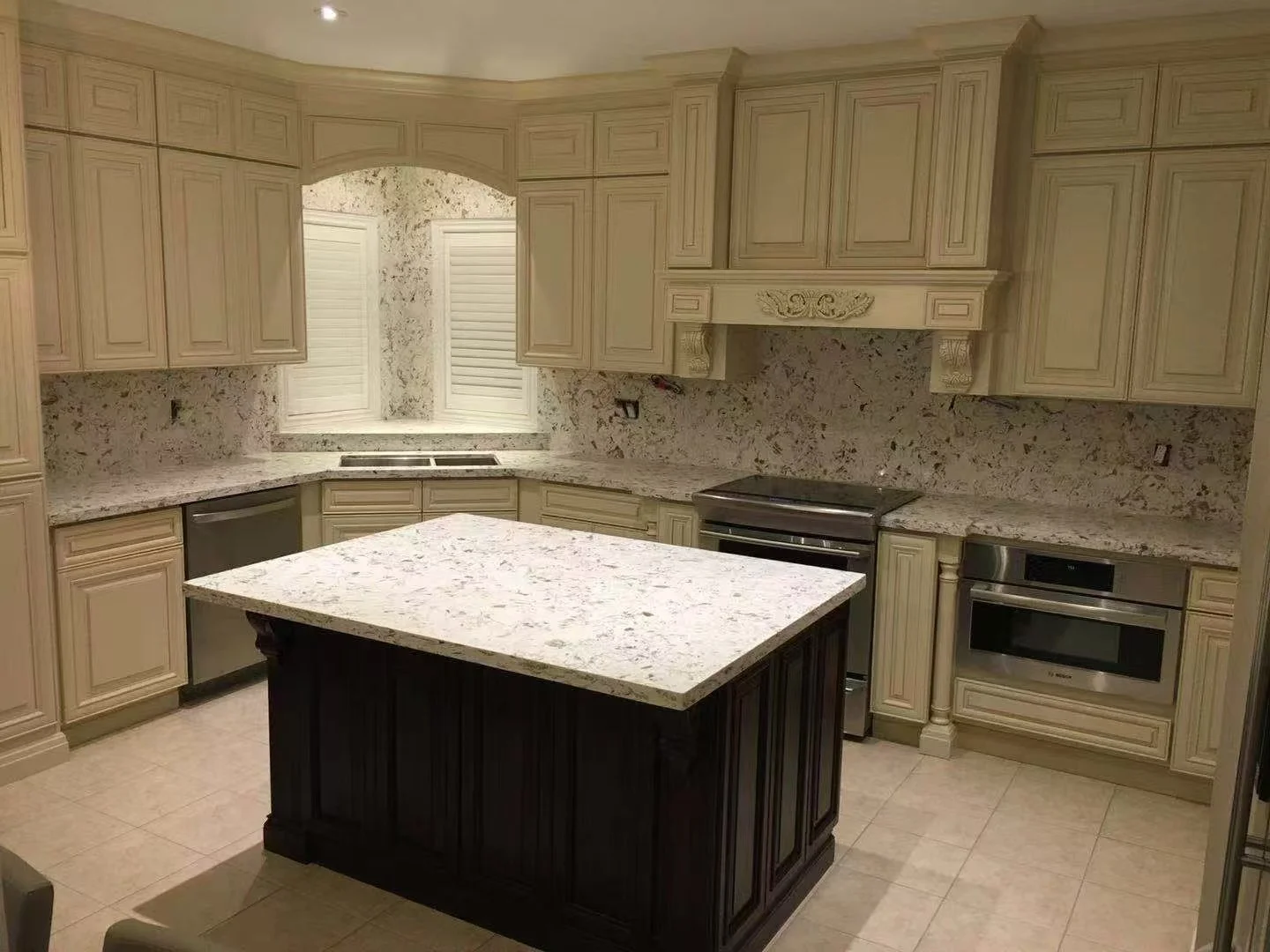Kitchen with cream-colored cabinets, granite countertops, an island with a dark wood base, stainless steel appliances, and a window with shutters.