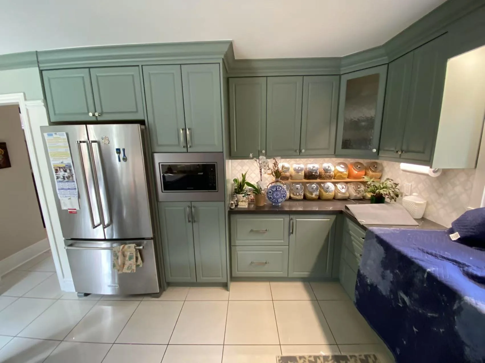 Kitchen with green cabinets, stainless steel refrigerator, microwave oven, and various spice jars on the countertop.