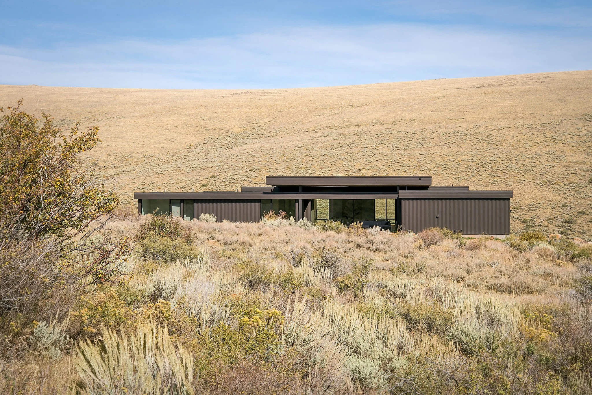 Low modern home with dark cladding set into a golden sagebrush hillside, Boar Shoat, Bear Lake, Idaho.