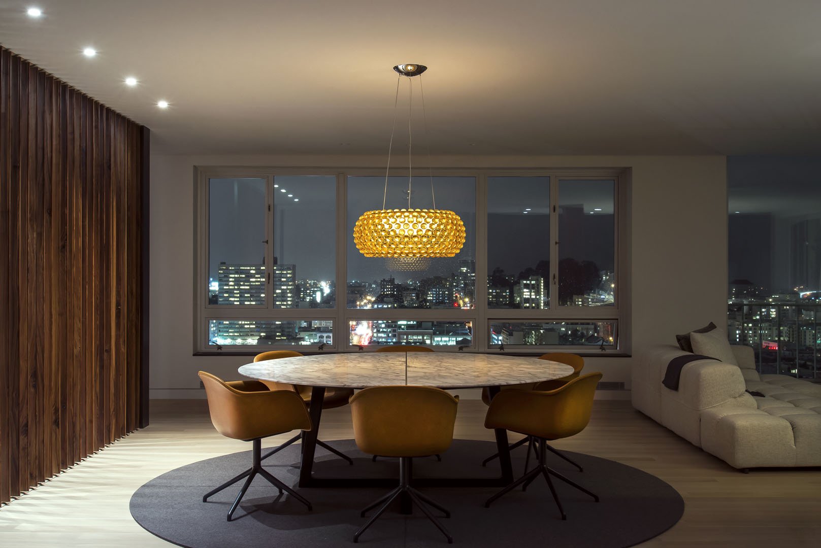 Modern dining room with a round marble table, sculptural pendant light, and city skyline views at night, Nob Hill, San Francisco, California.