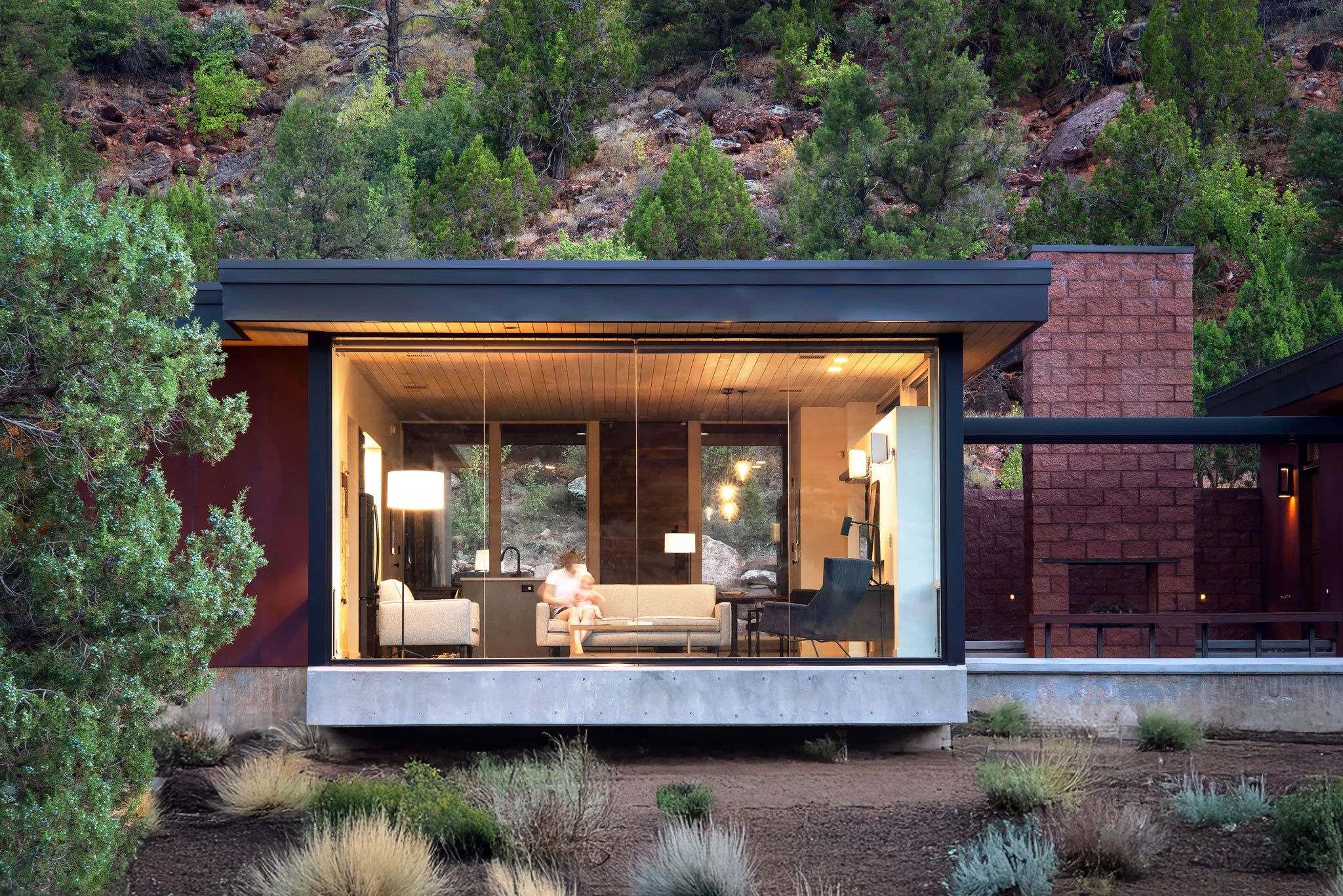 Modern home with an open glass living space and brick walls below a Zion canyon hillside, Watchman, Springdale, Utah.