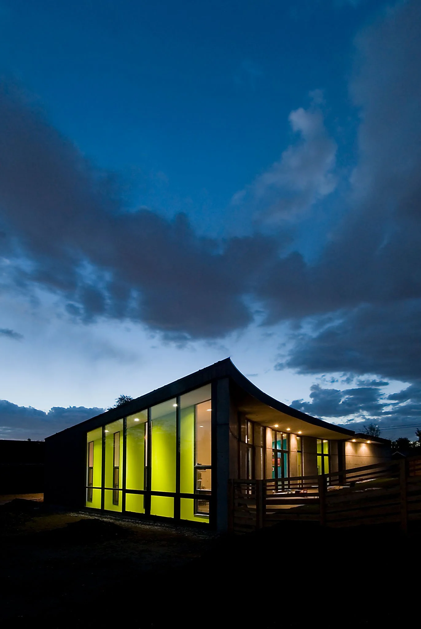 Modern home with a sweeping curved roofline glowing at dusk through walls of glass, Thorn, Salt Lake City, Utah.