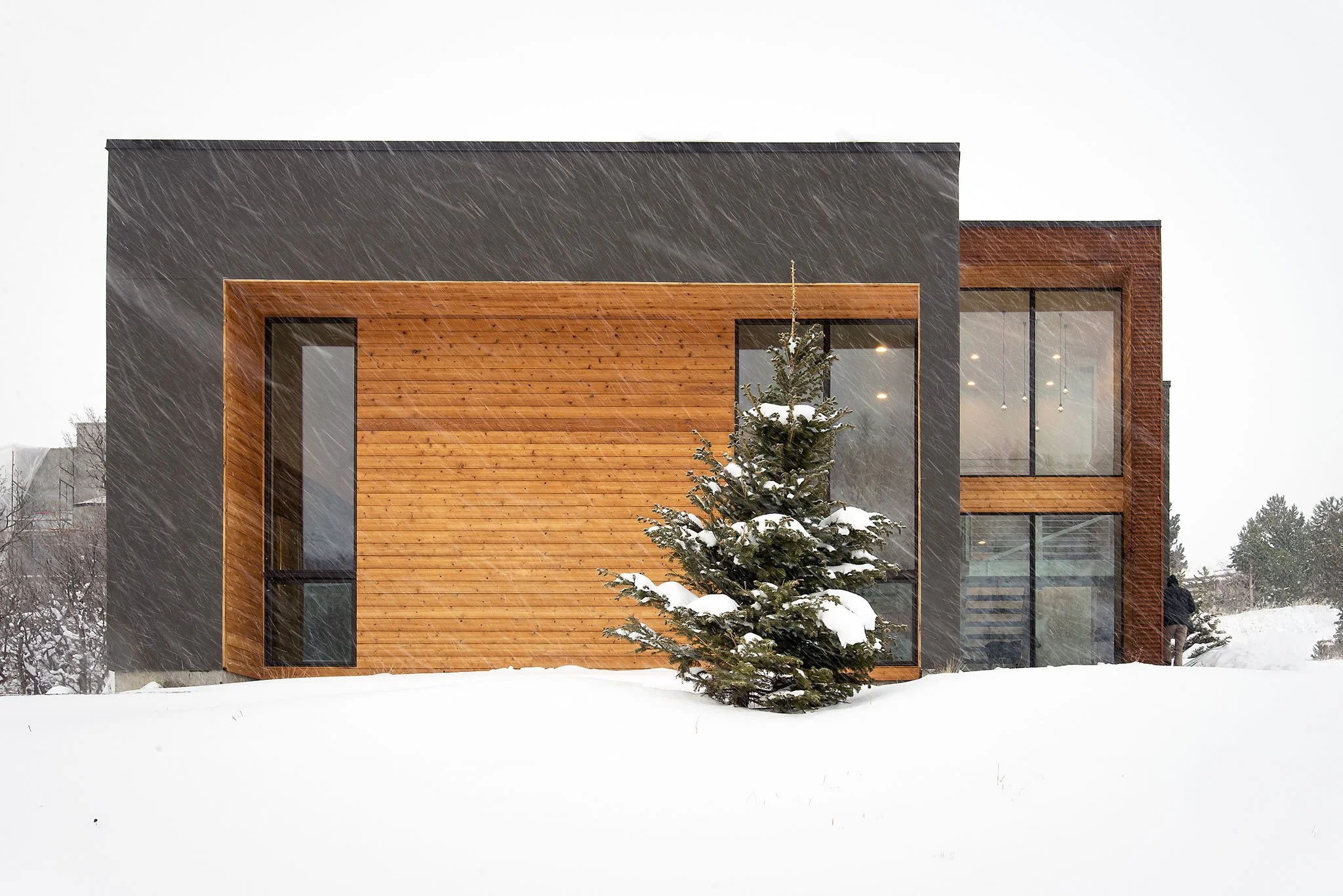 Modern home with wood and dark-clad volumes and tall glass during a snowfall, Emigration, Salt Lake County, Utah.