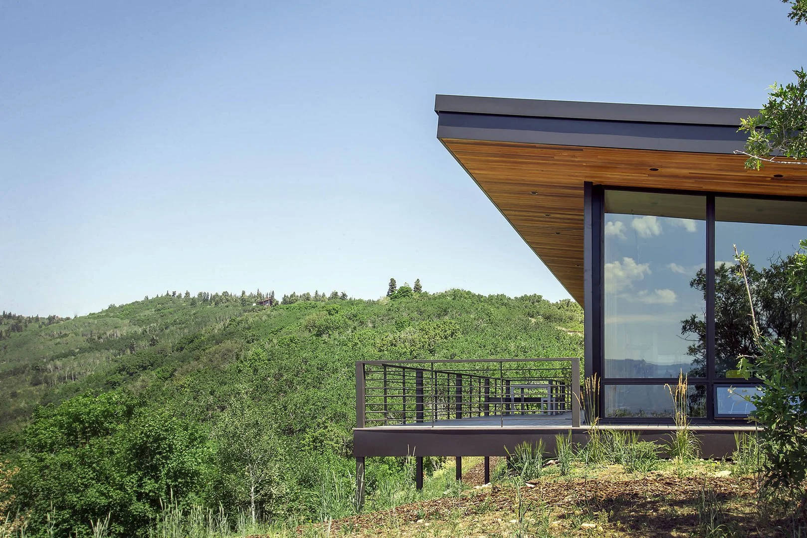 Cantilevered modern home with a wood soffit and a steel-railed deck overlooking the green Park City hills, Red Hawk, Park City, Utah.
