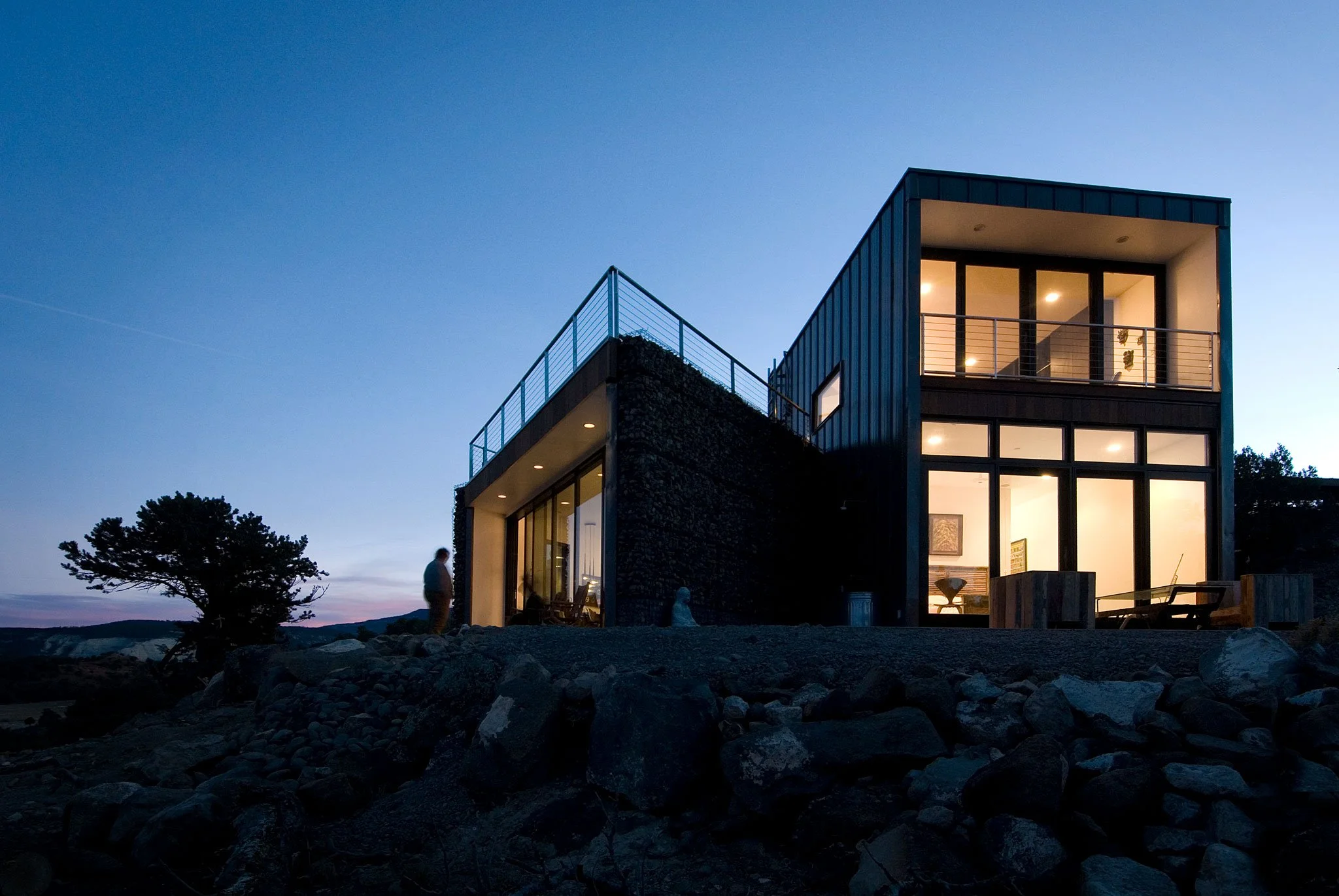 Modern two-volume desert retreat with a stone base glowing at dusk, Buddhist Retreat, Torrey, Utah.