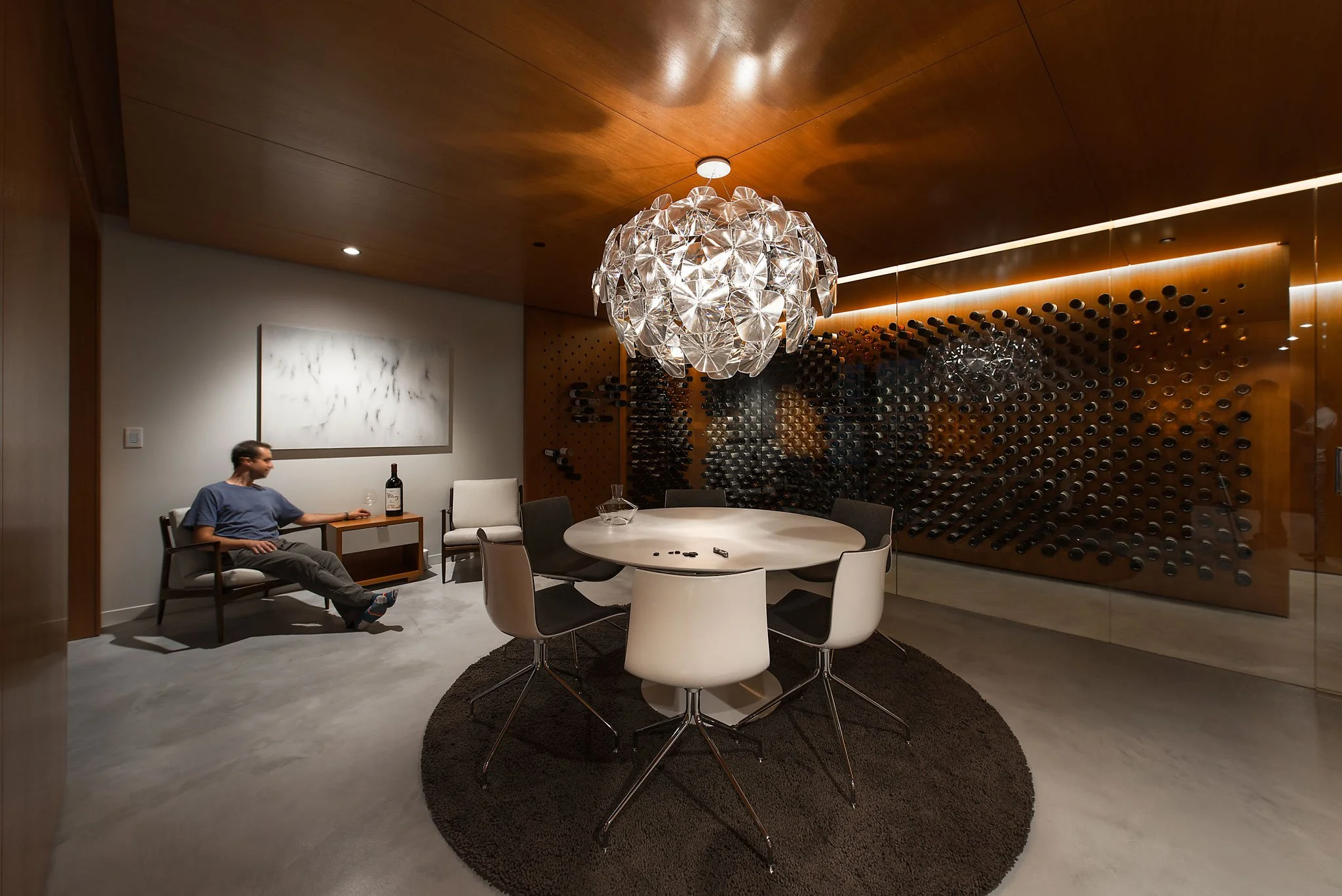 Wine tasting room with a sculptural chandelier and a perforated wood bottle-storage wall, Wine Cellar, Ogden, Utah.