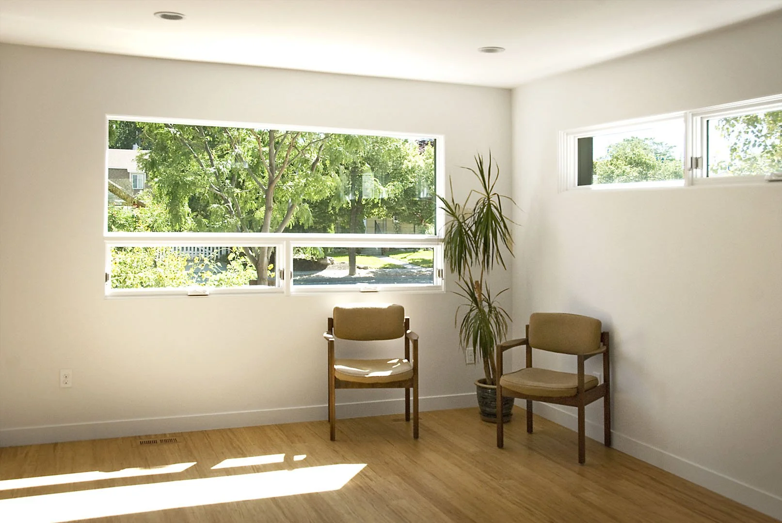 Bright corner living space with wood floors and windows opening onto leafy greenery, 600 East, Salt Lake City, Utah.