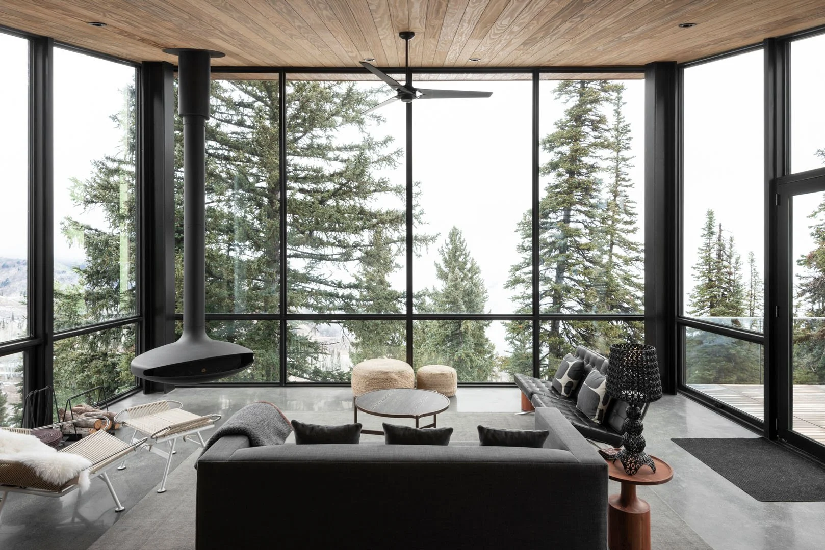 Living room with a suspended fireplace and walls of glass framing the forest, Ridge Nest, Powder Mountain, Utah.